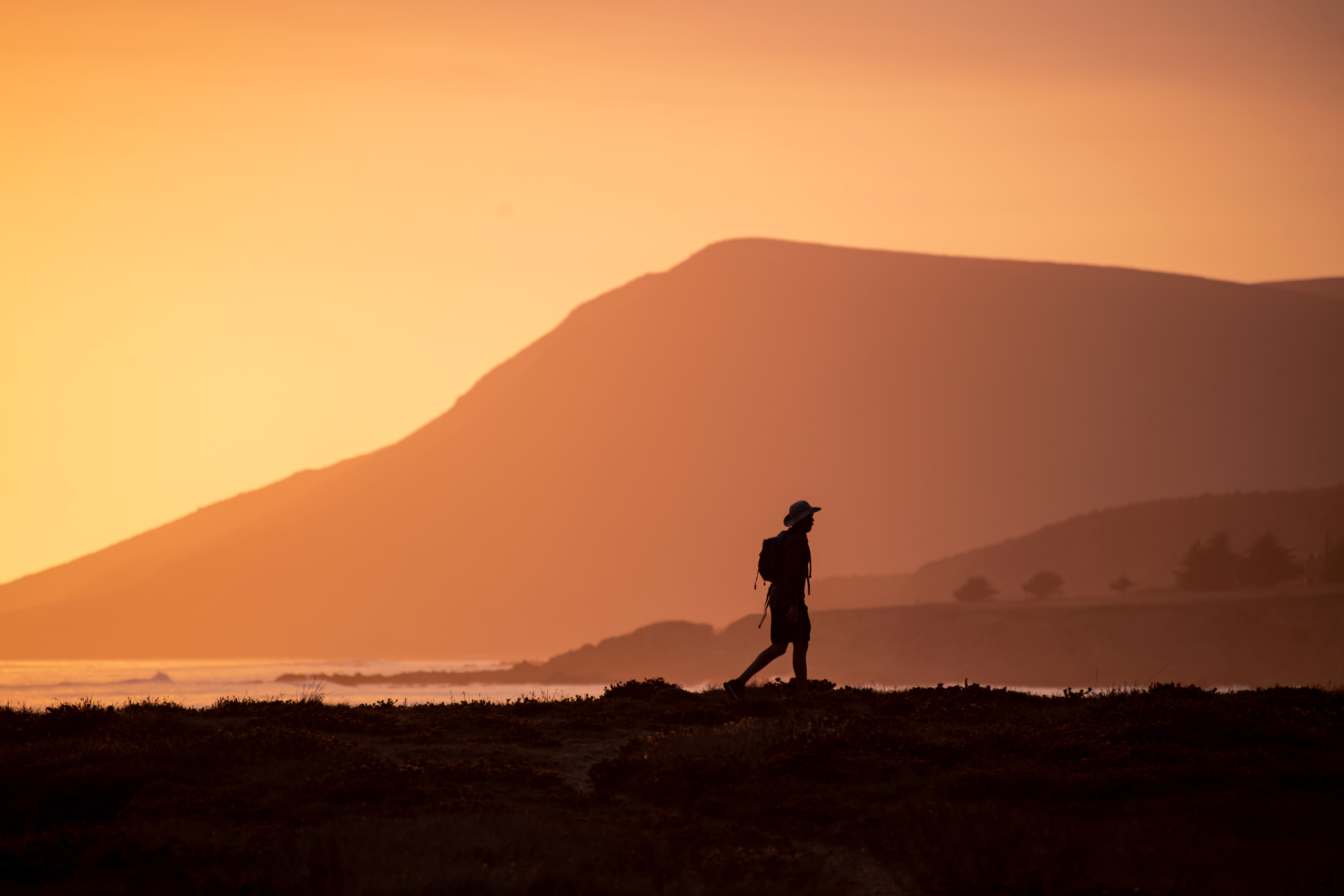 A silhouette of a person walking towards inland from the coast during a sunset.