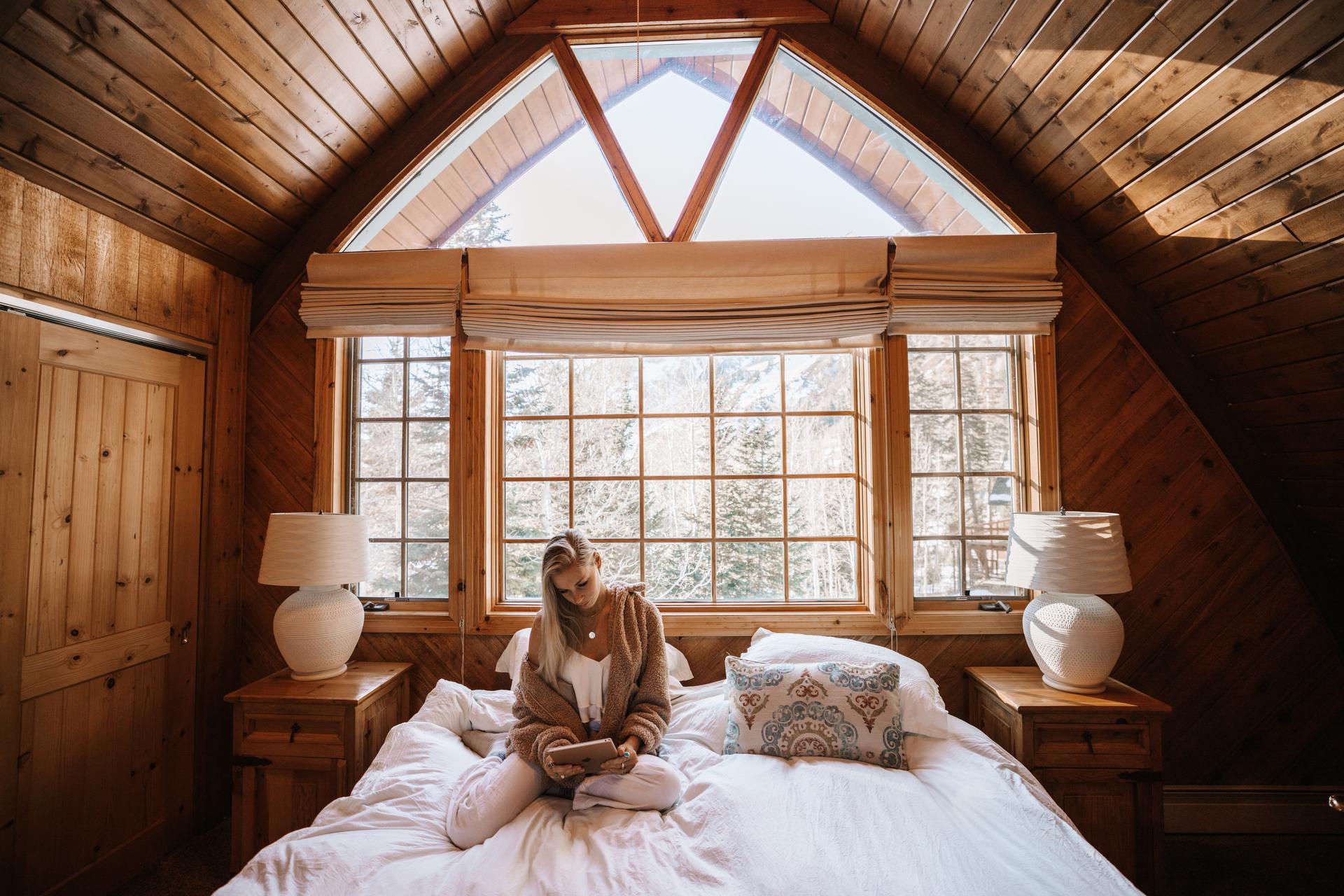 Woman looking at an ipad on a bed in a cabin.