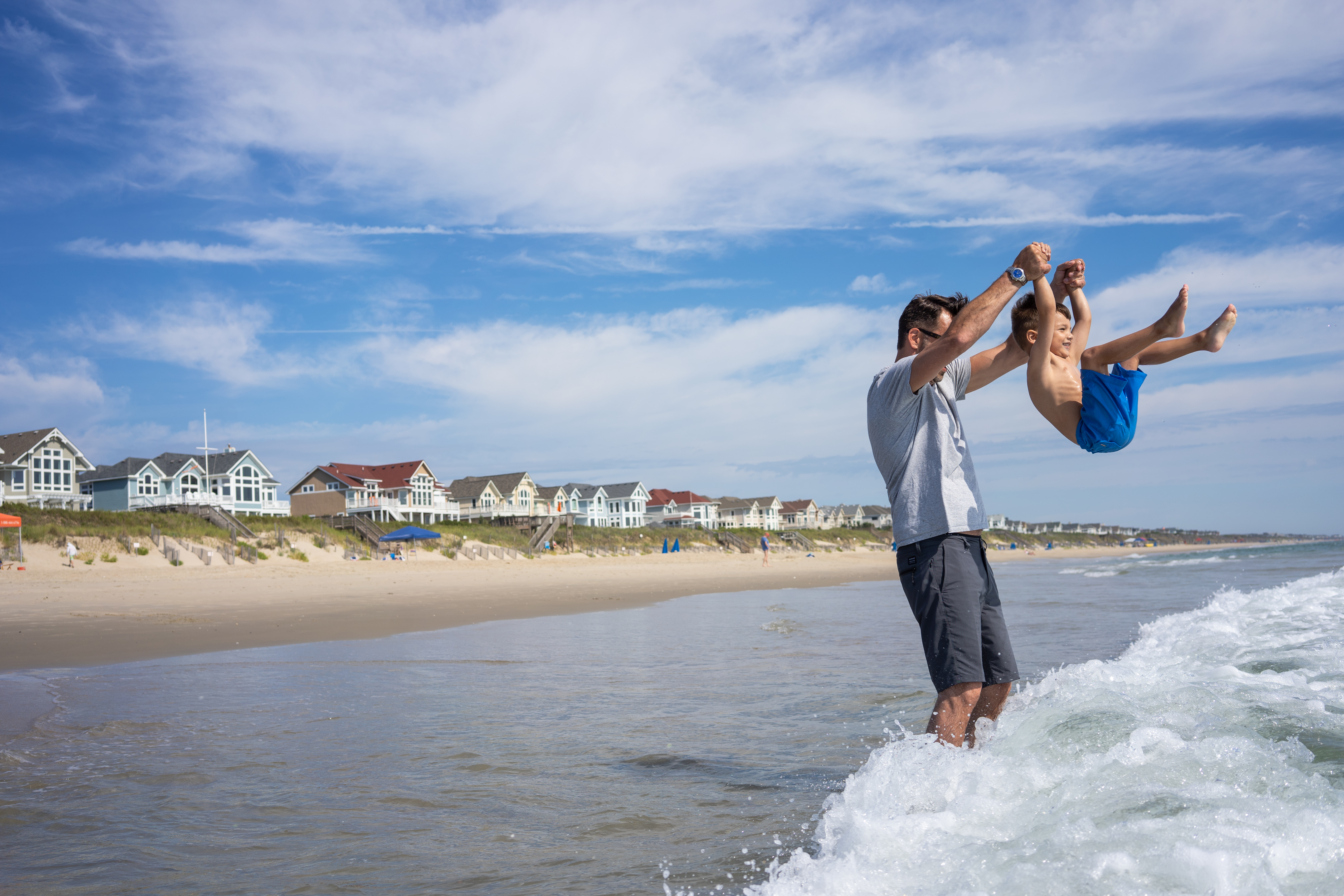 Man picking up a little boy in the surf in front of oceanfront homes in Corolla, North Carolina