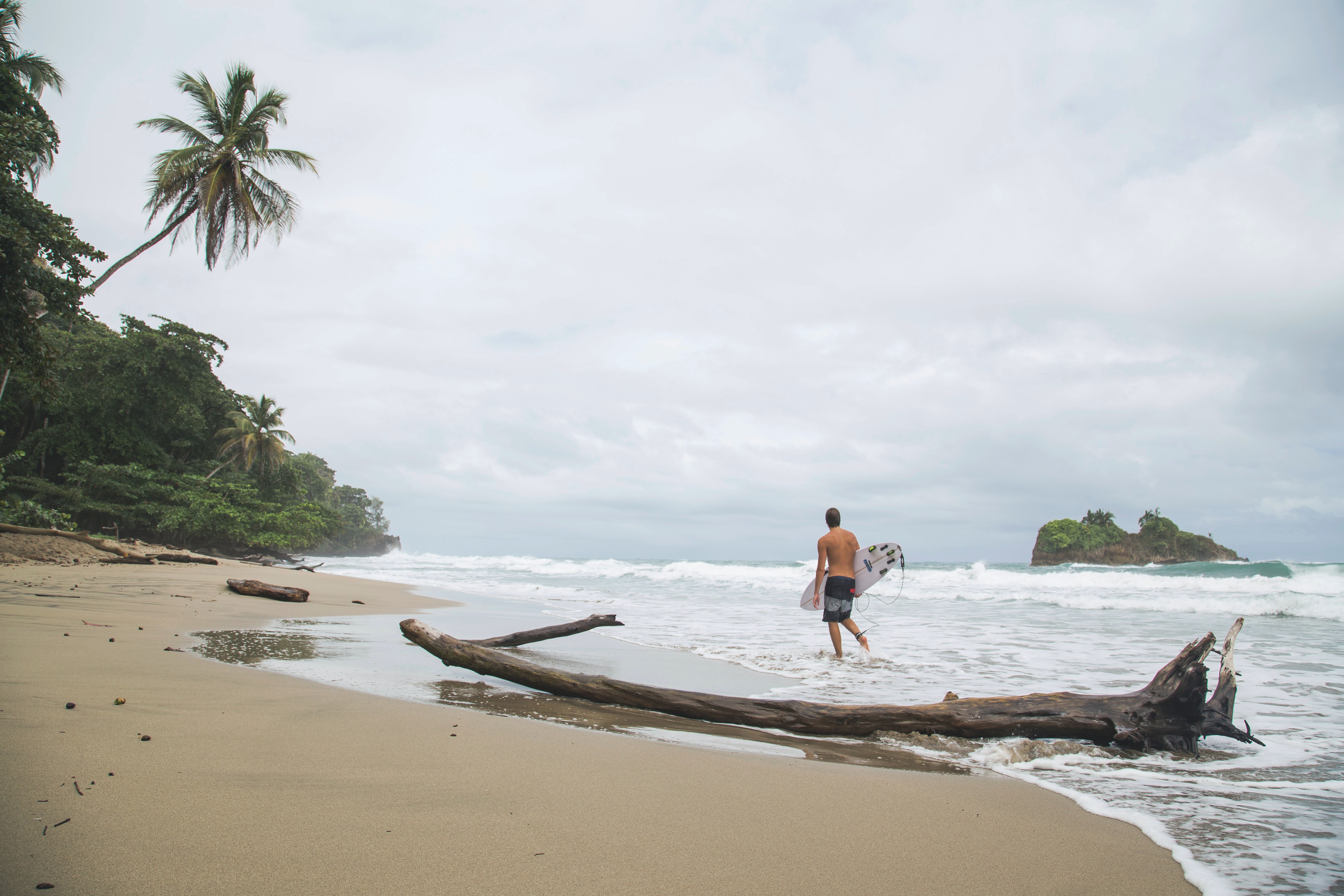 person holding a surfboard walks along a Costa Rica beach