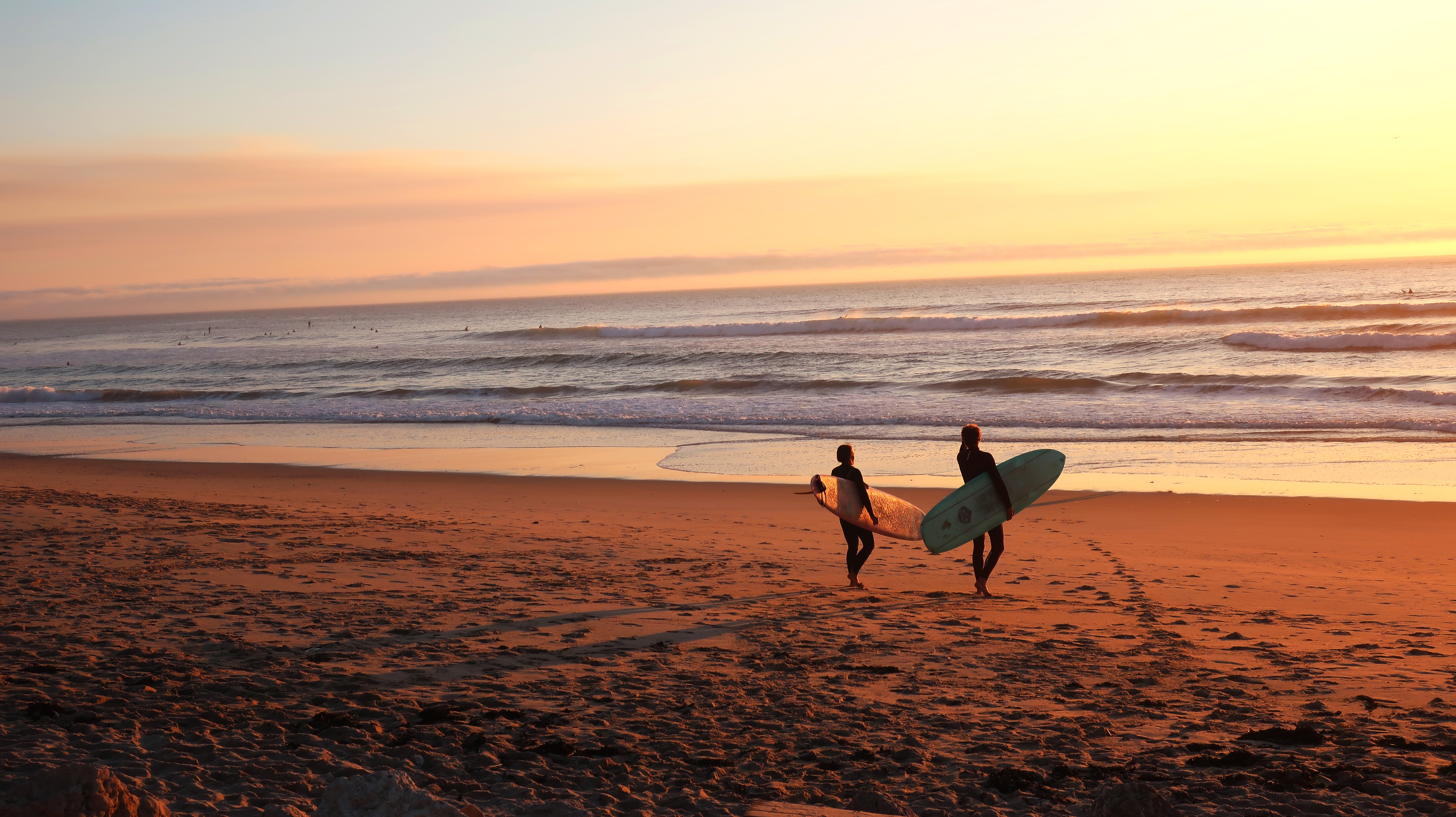 two surfers walk towards the water with their surfboards