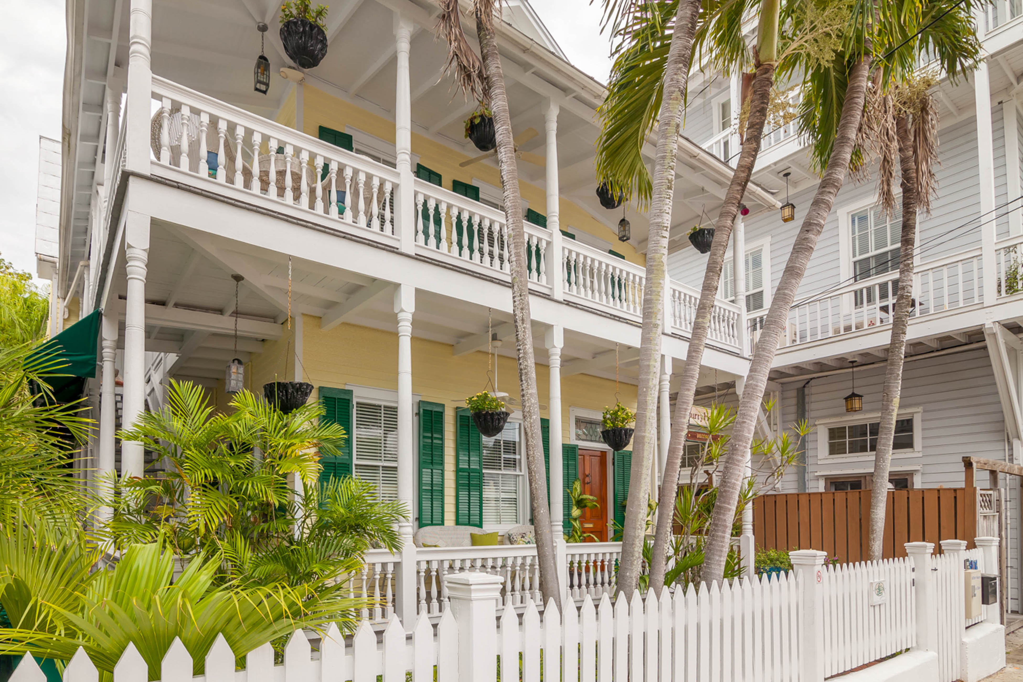 Large two story yellow and white vacation rental with white picket fence and palm trees.