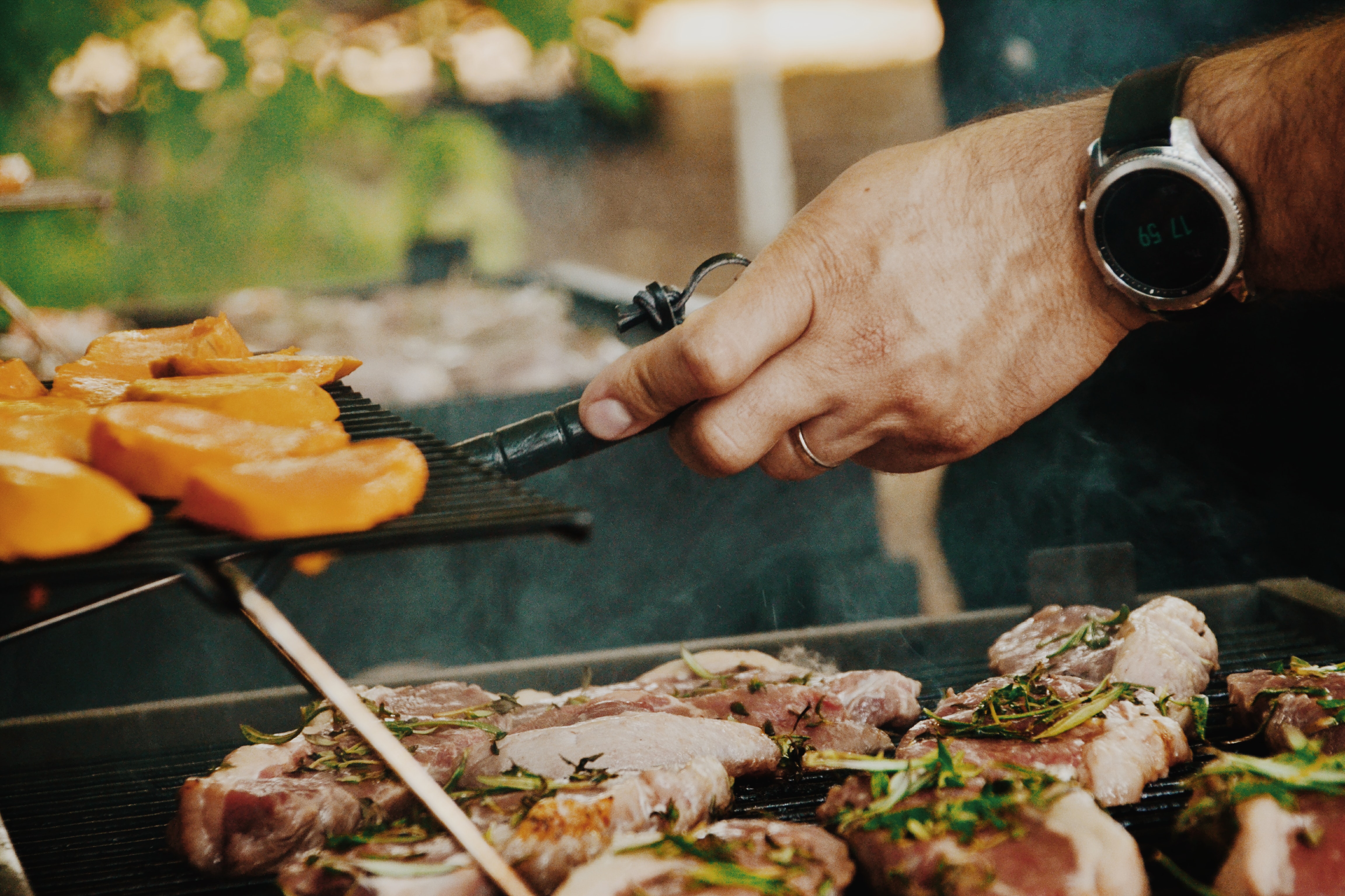 A person cooking steak and vegetables on an outdoor grill at a vacation rental.