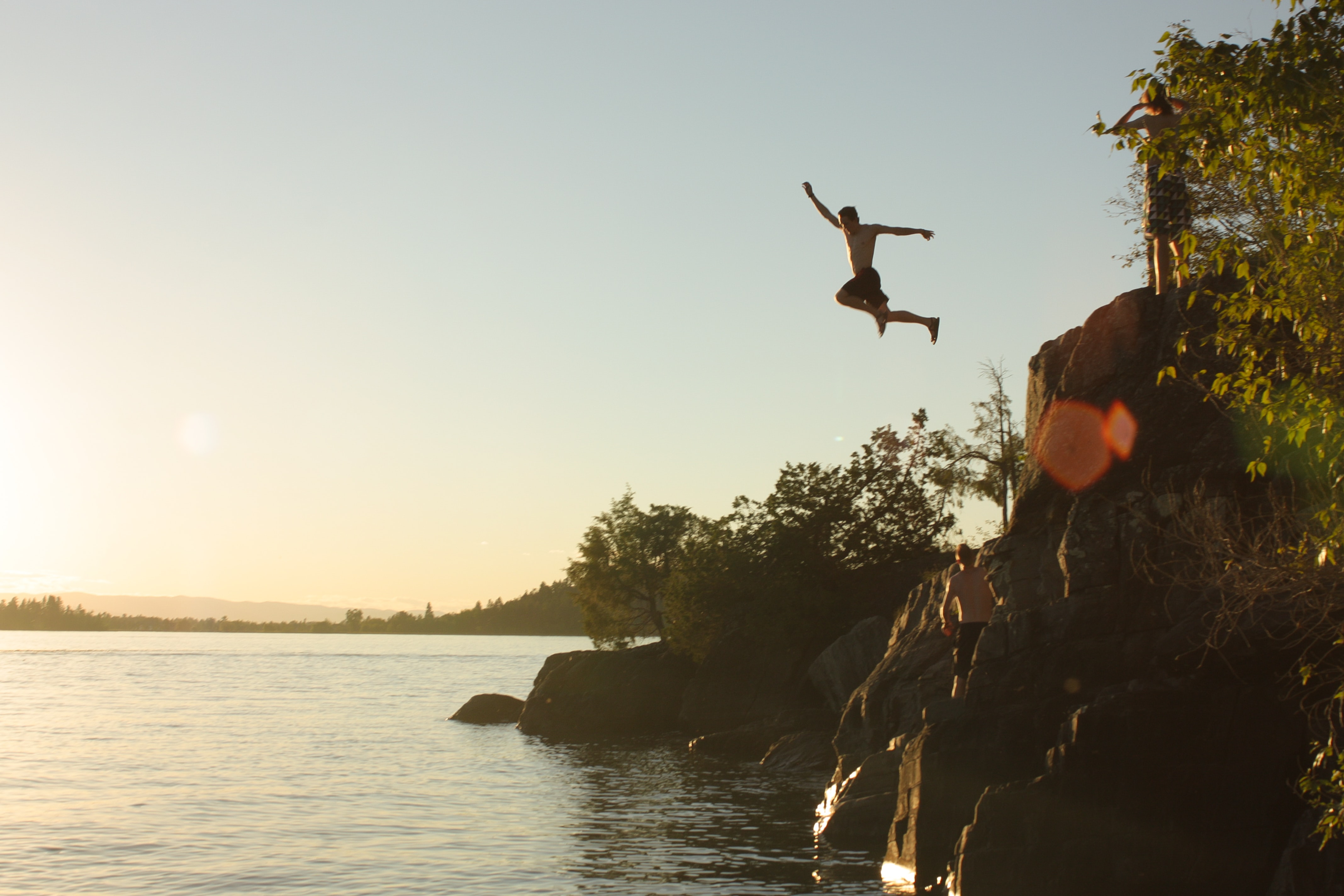 People cliff jumping into Flathead Lake during a sunset