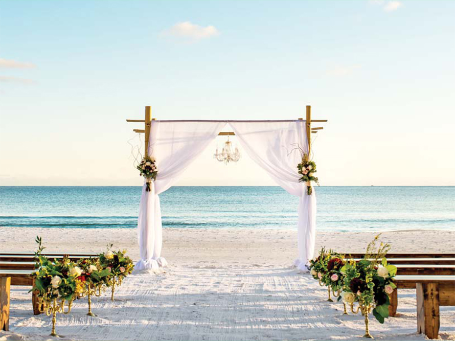 Wedding ceremony on the beach in Florida with a wooden arbor decorated with white drapes and flowers