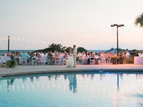 Bride and groom dancing by an outdoor pool while guests watch at their tables