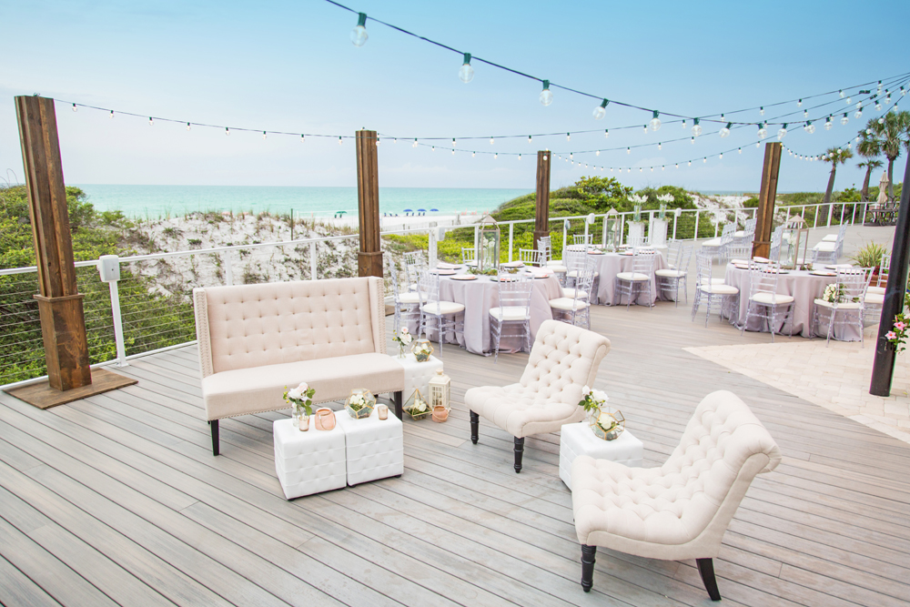 Outdoor lounge chairs with wedding decorations on an outside deck with an ocean view