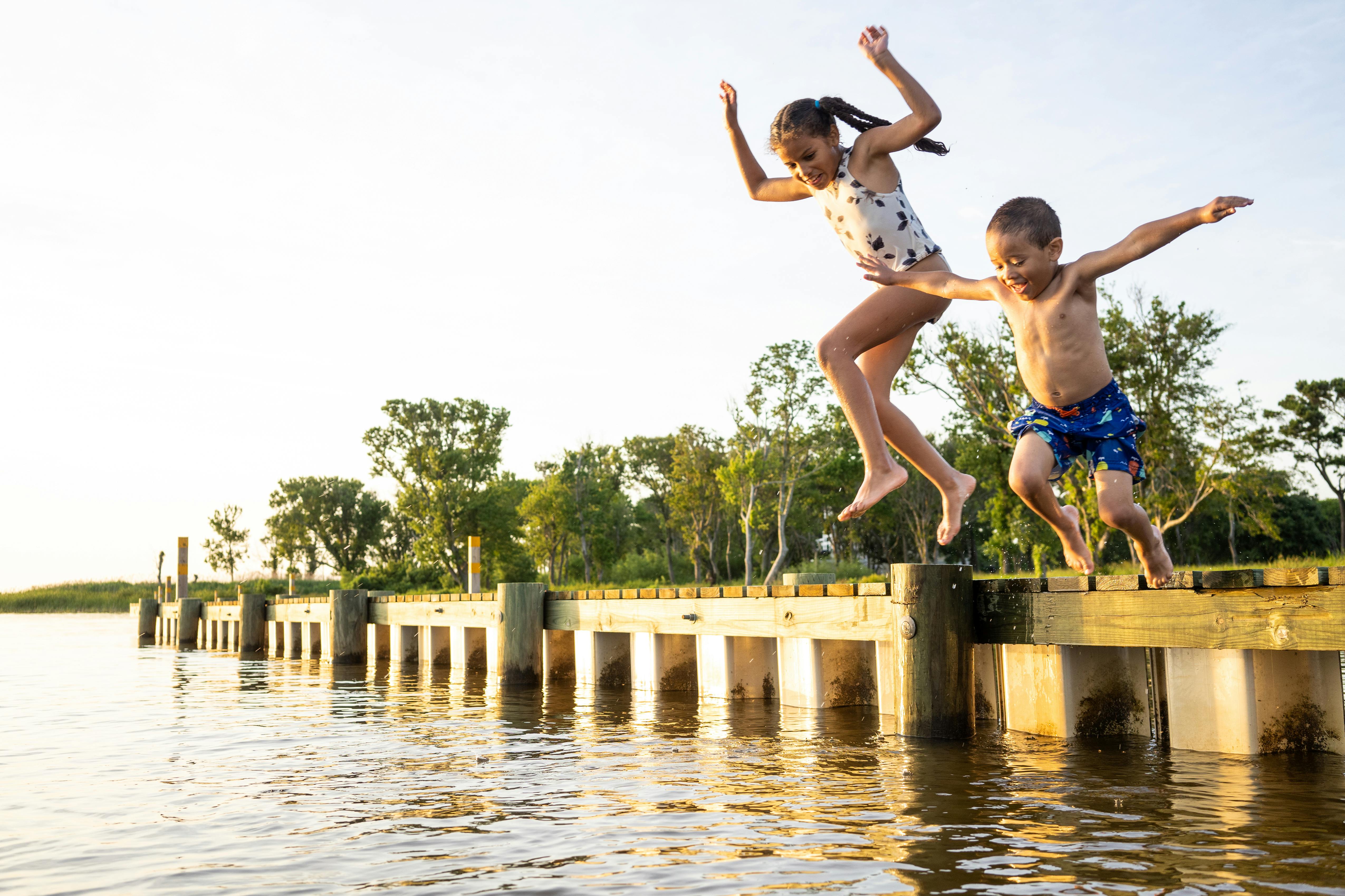 Two kids jumping off a dock into the water