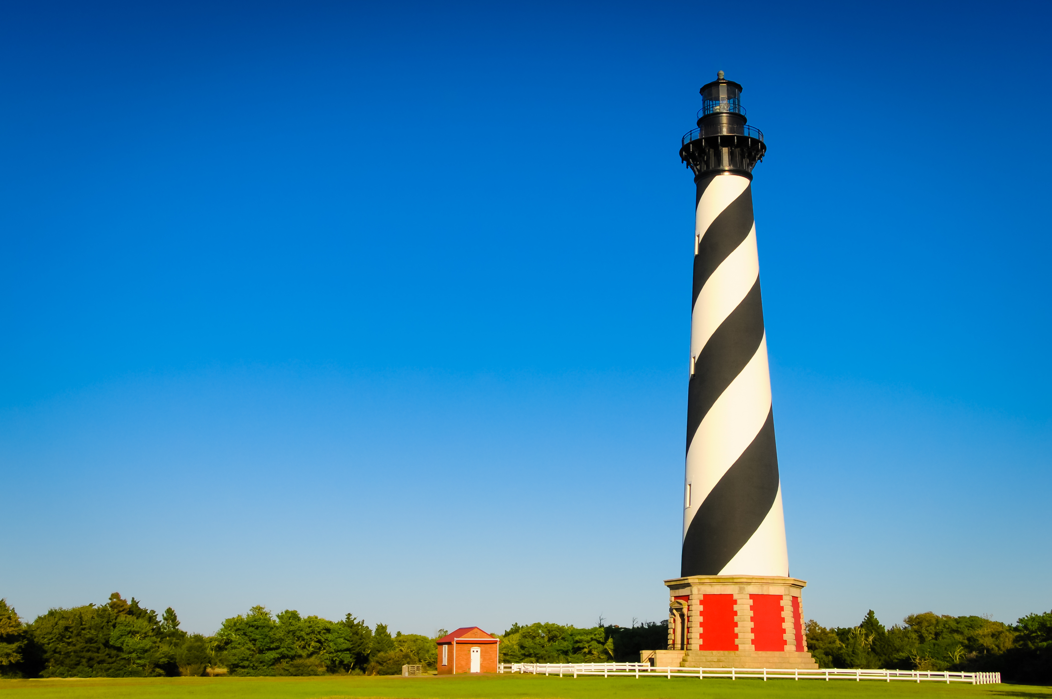 A black and white lighthouse in an open green field with trees and a red barn during the day.