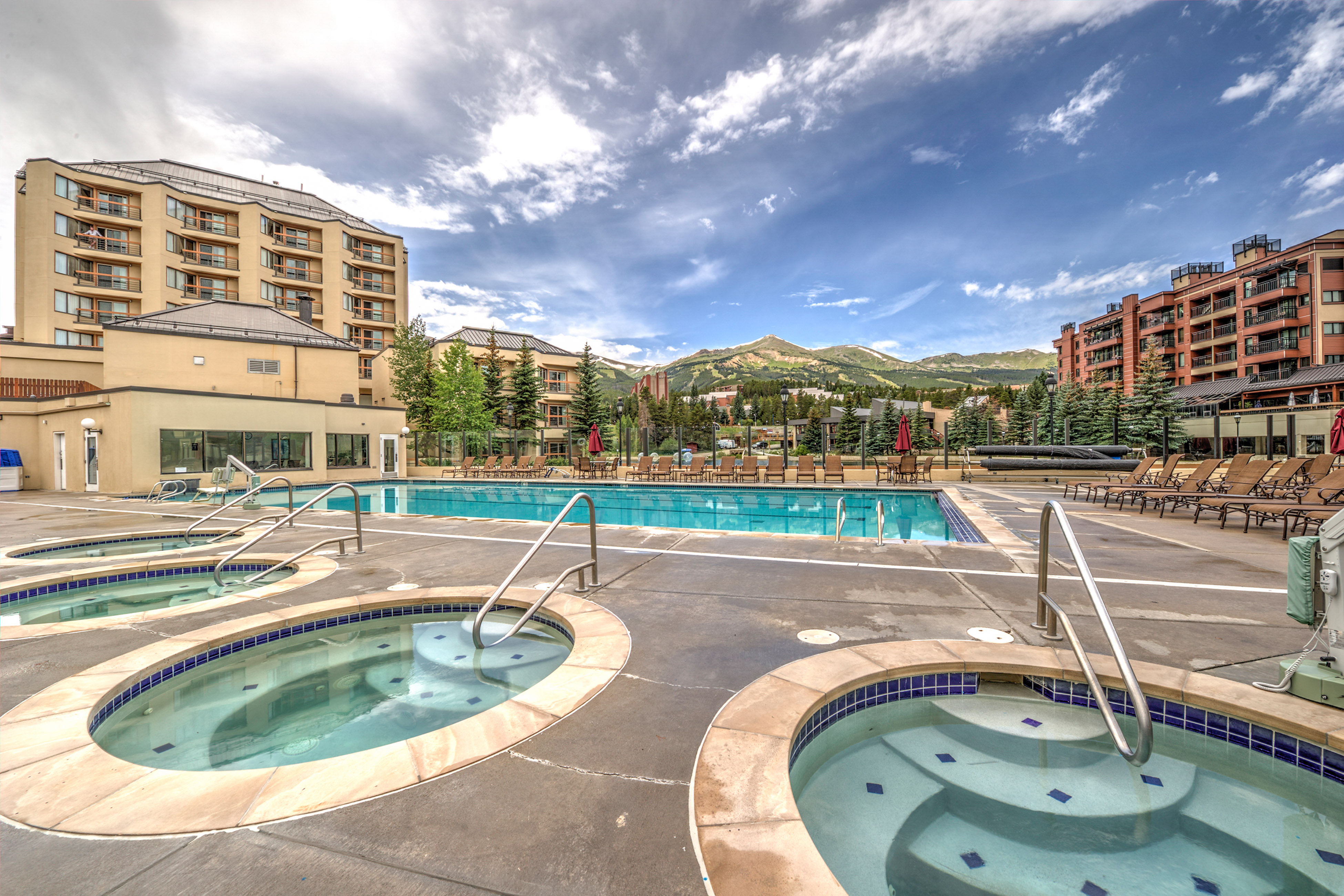 Large swimming pool and spa pools at a resort with mountains in the background.