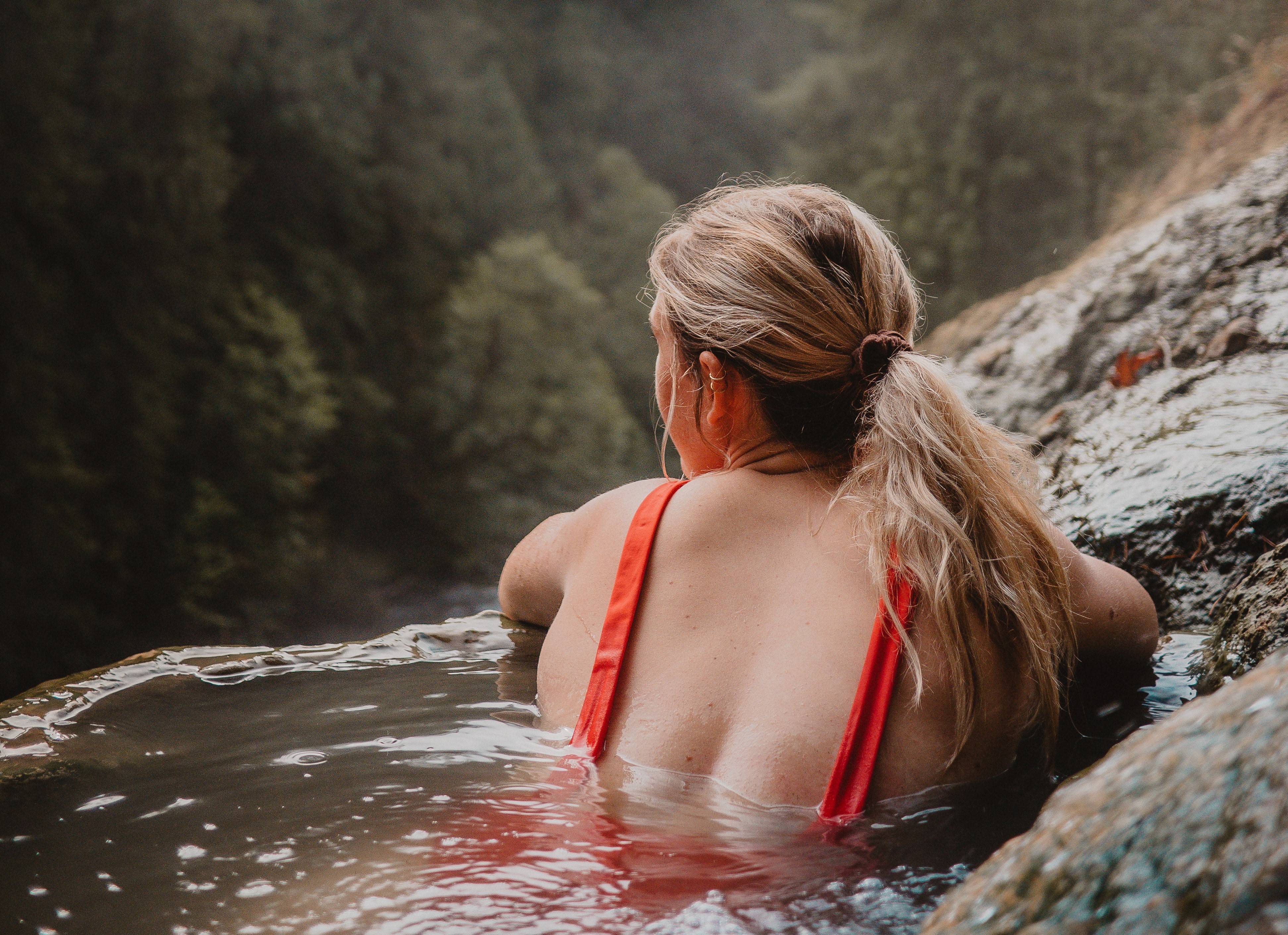 A woman in a hot spring looking towards a forest in McCall, ID.