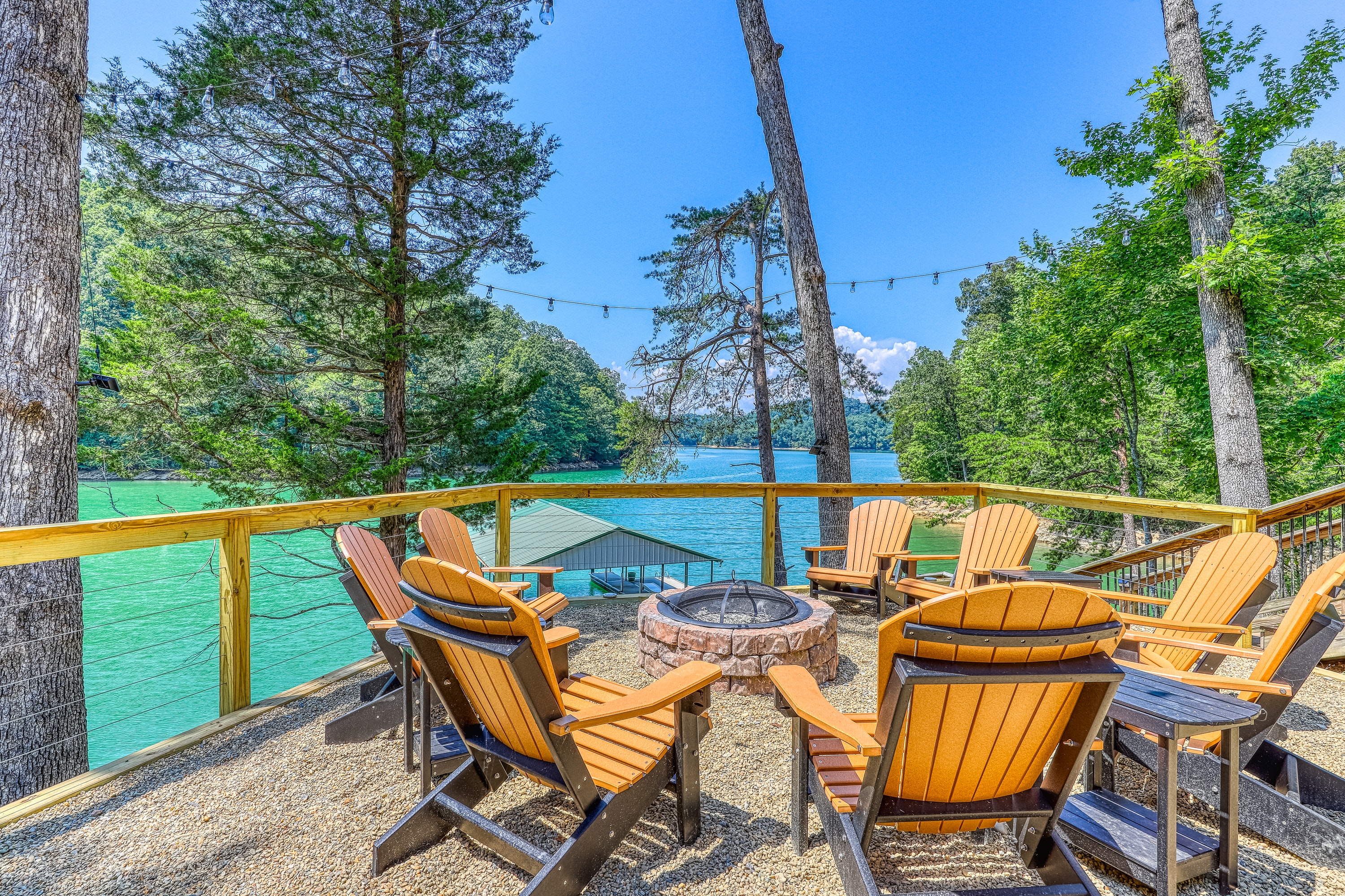 adirondack chairs surround a firepit that overlooks a lake and dock below
