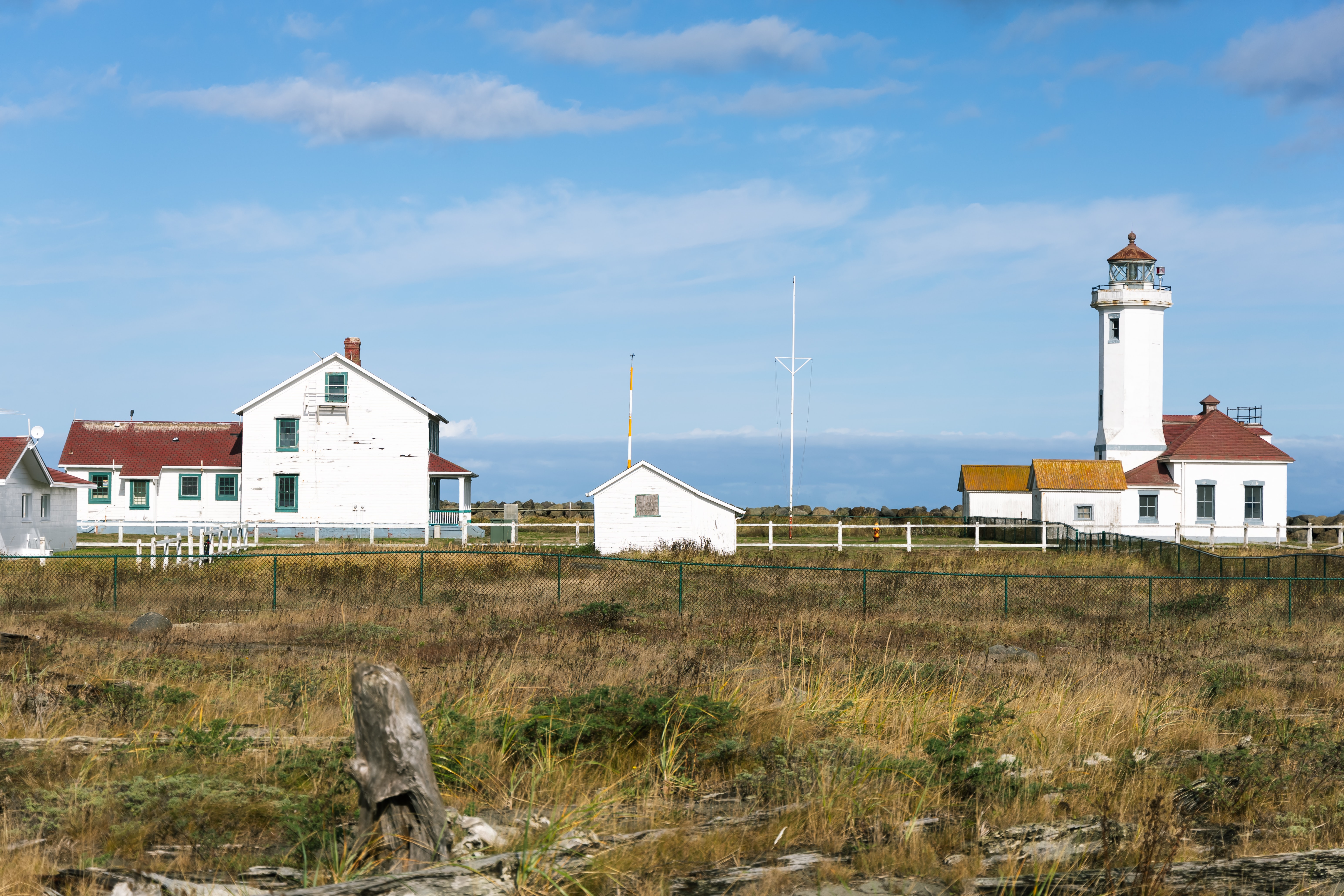 A white lighthouse and a home with a large field overlooking the coast during the day.