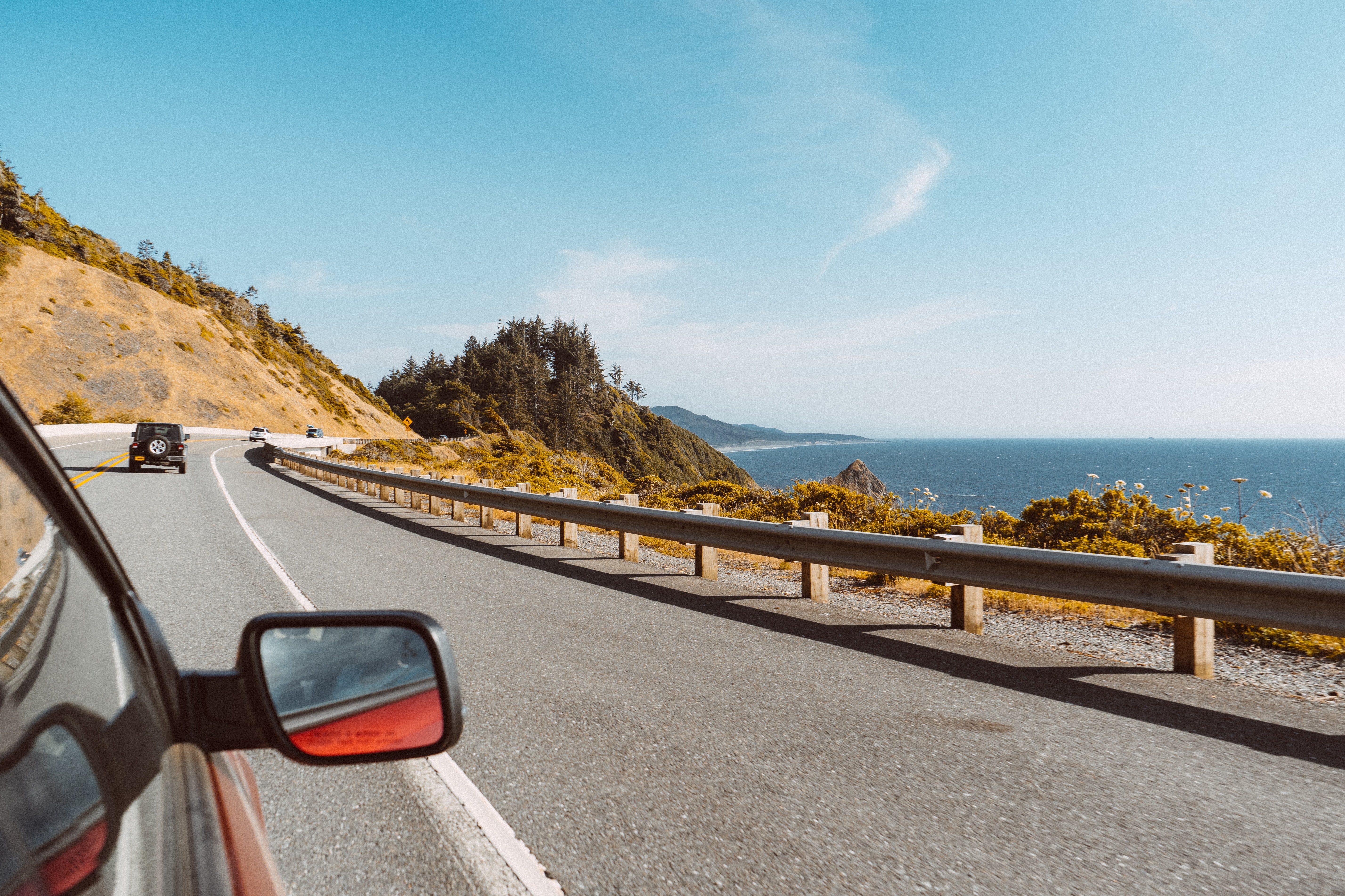 Car driving along the Pacific coast highway with a view of the ocean on a sunny day.