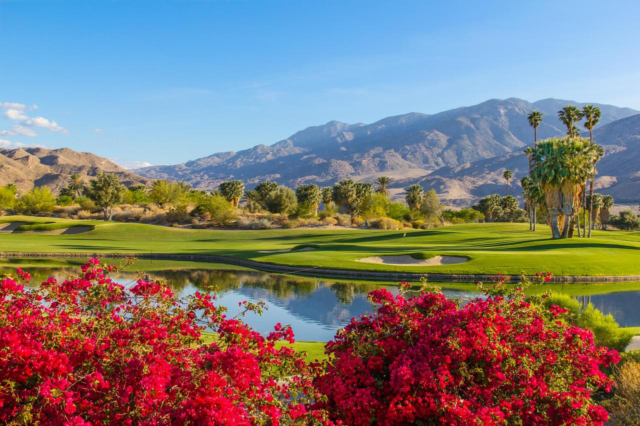 Palm Springs golf course with flowers in the foreground and mountains in the background. There's a water feature, sand trap and tree hazards too.