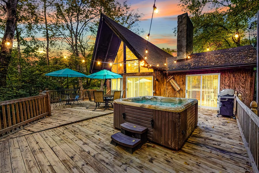 string lights drape over the deck of a vacation rental in poconos with a hot tub and outdoor table