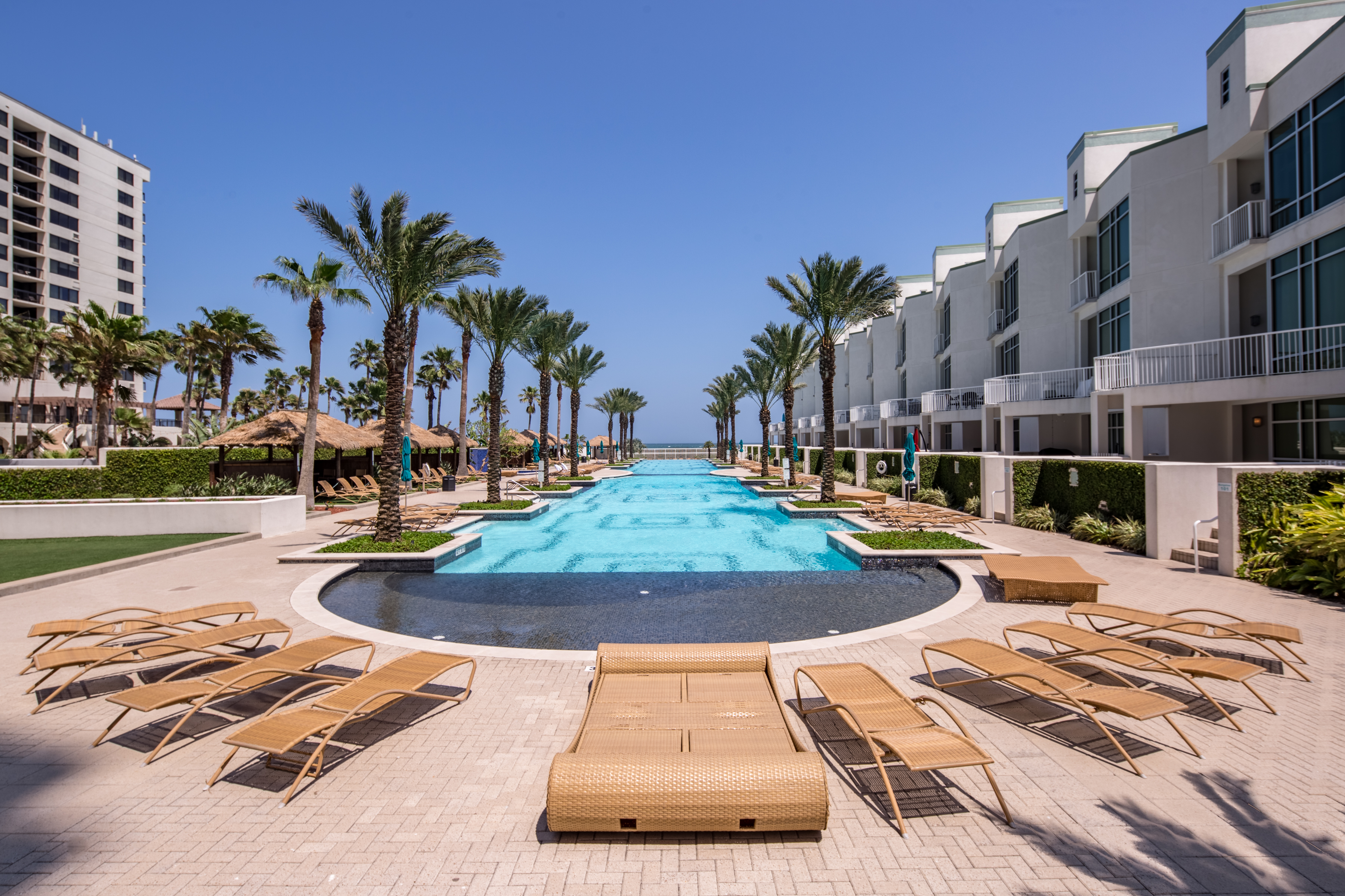 The pool lined with deck chairs and palm trees at a resort in South Padre Island.