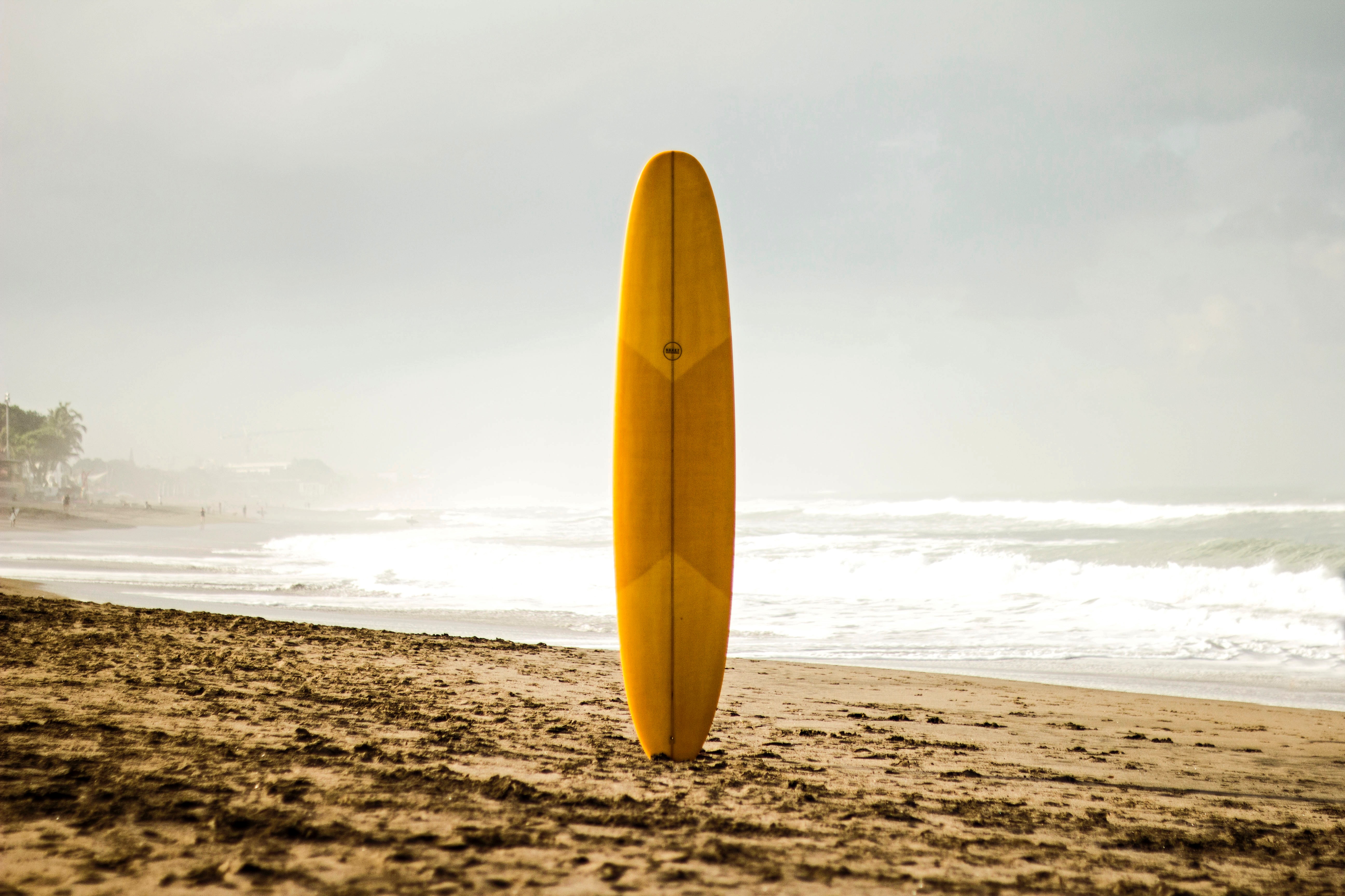 Surfboard sticks in the sand while waves crash