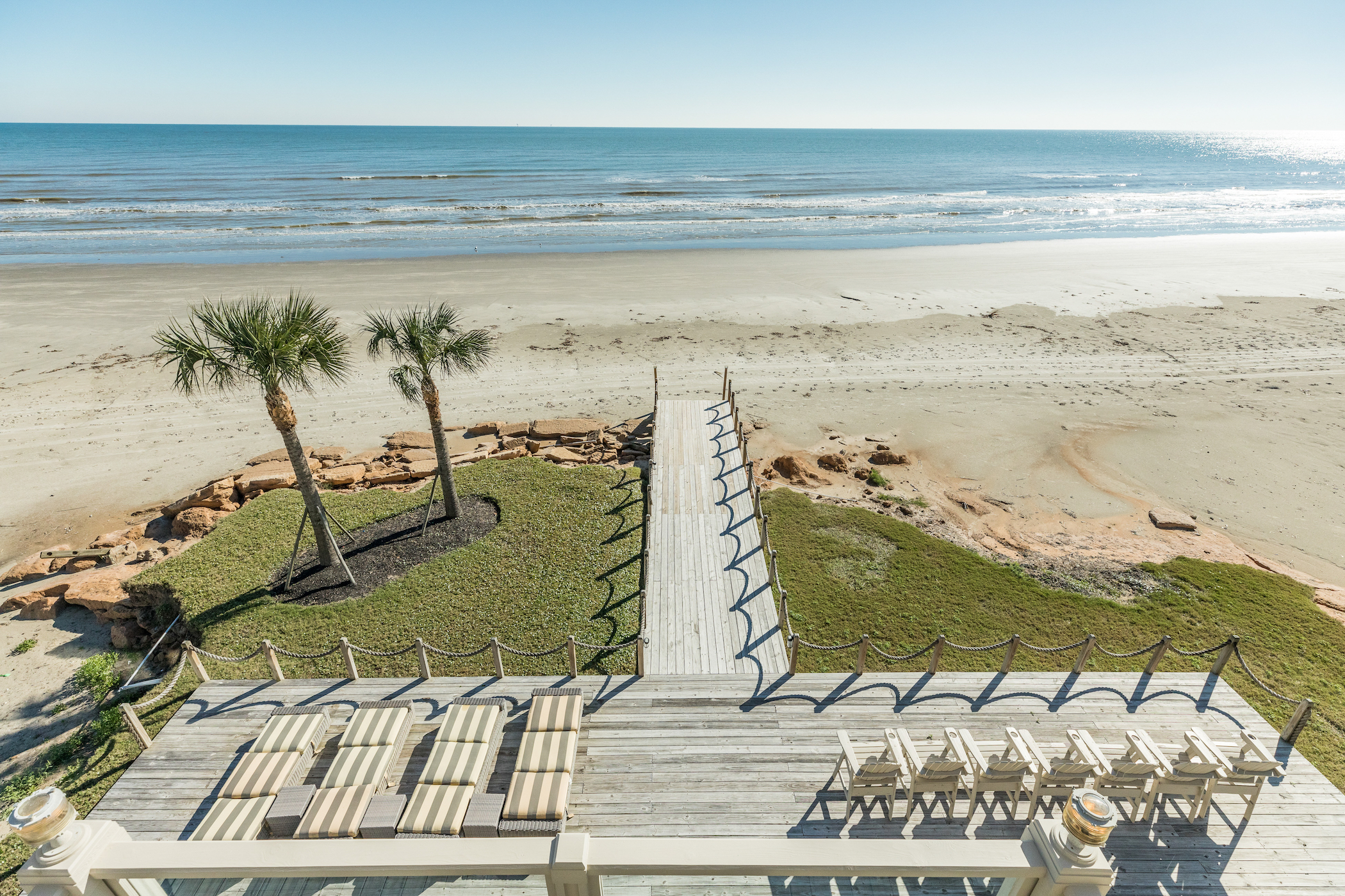 A deck of a vacation rental in Galveston leading to the beach with chairs.