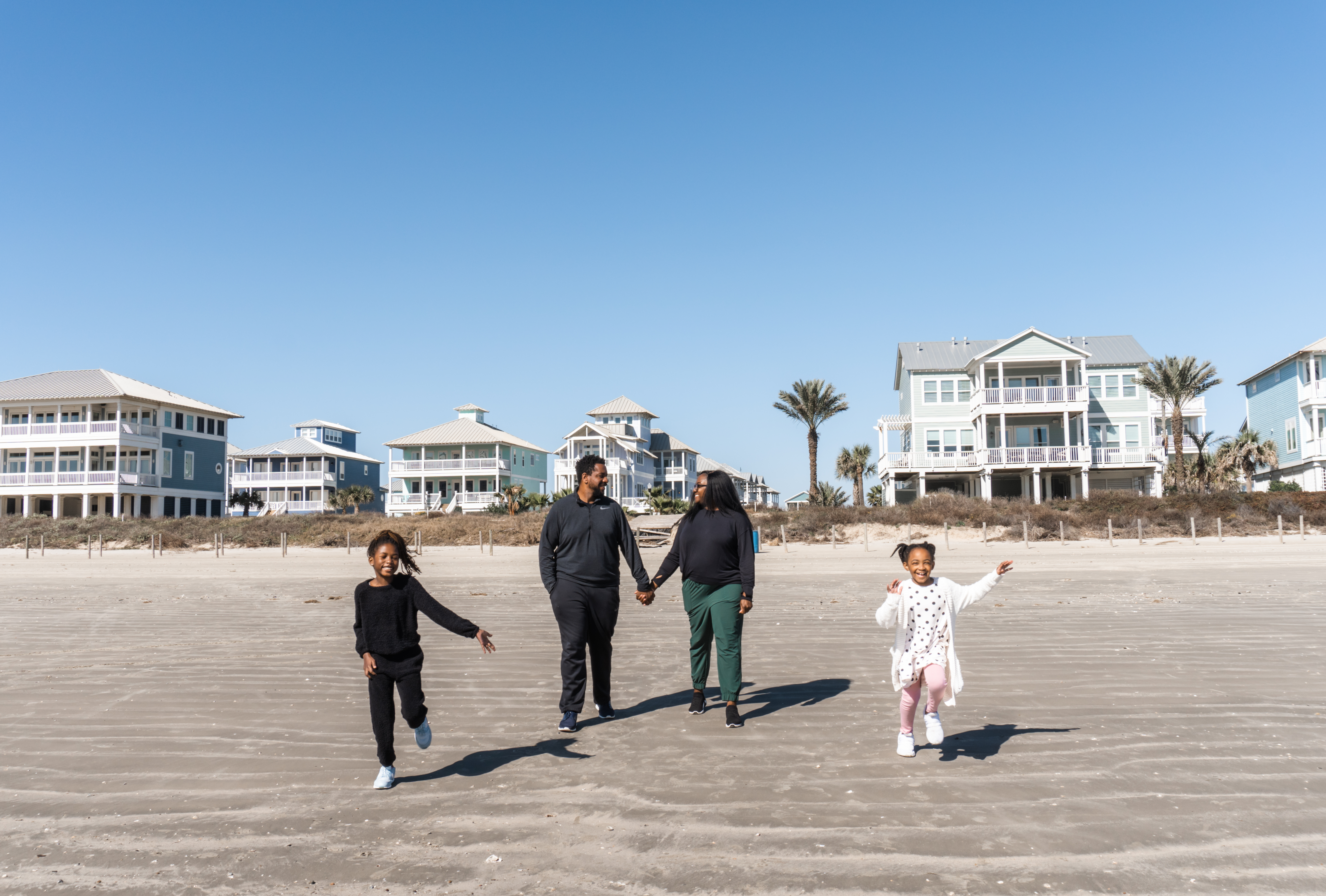 kids run on the beach while parents hold hands