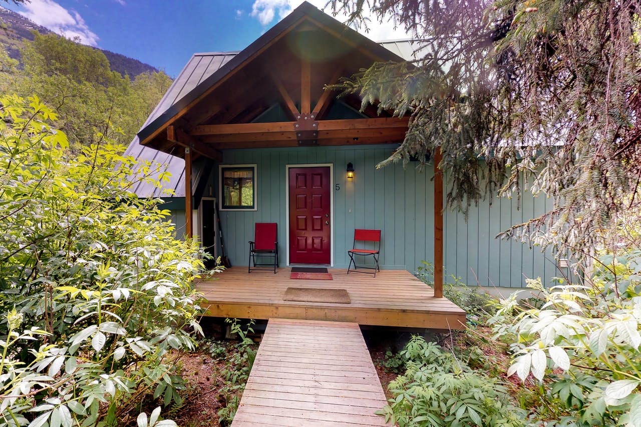 a girdwood cabin with a red door and red chairs on the front porch