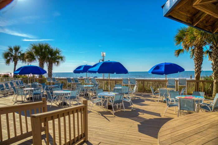 View of beach from Bay Watch Resort deck filled with dining tables and chairs