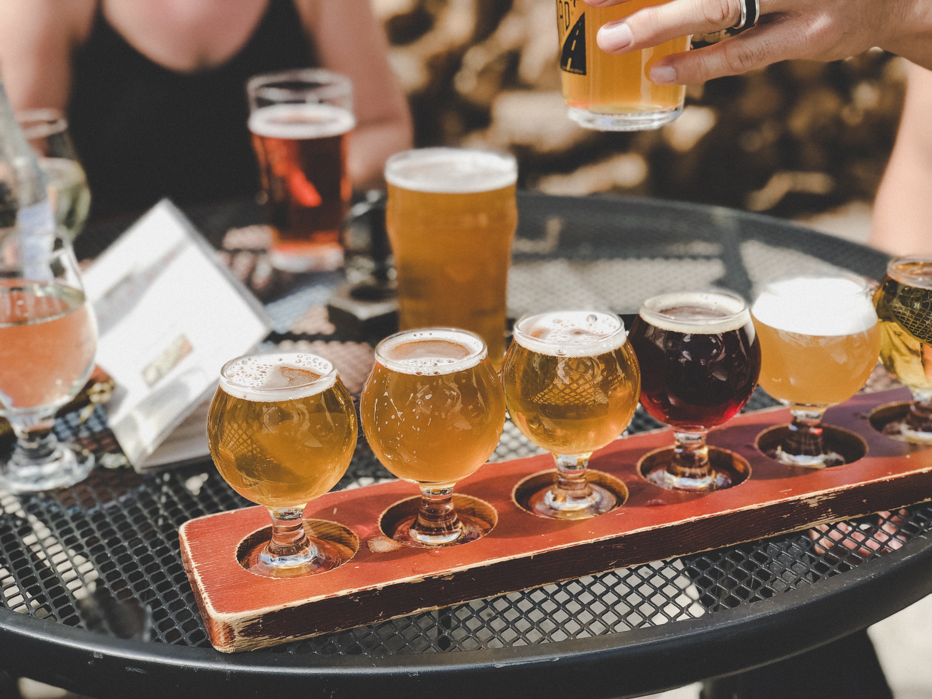 A flight of different beers being served to an outdoor table.