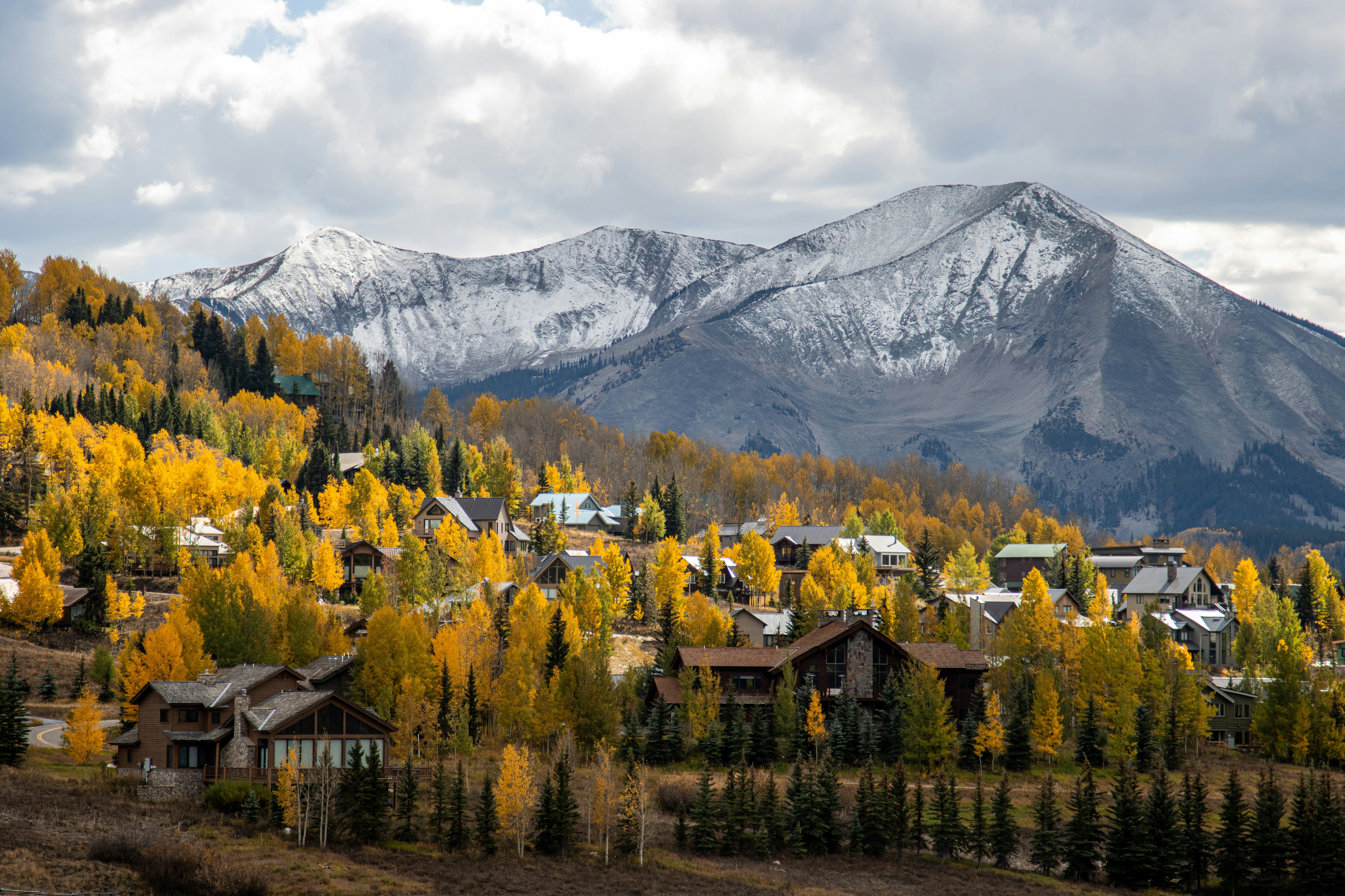 fall landscape of cabins and homes surrounded by golden trees and snowy mountains