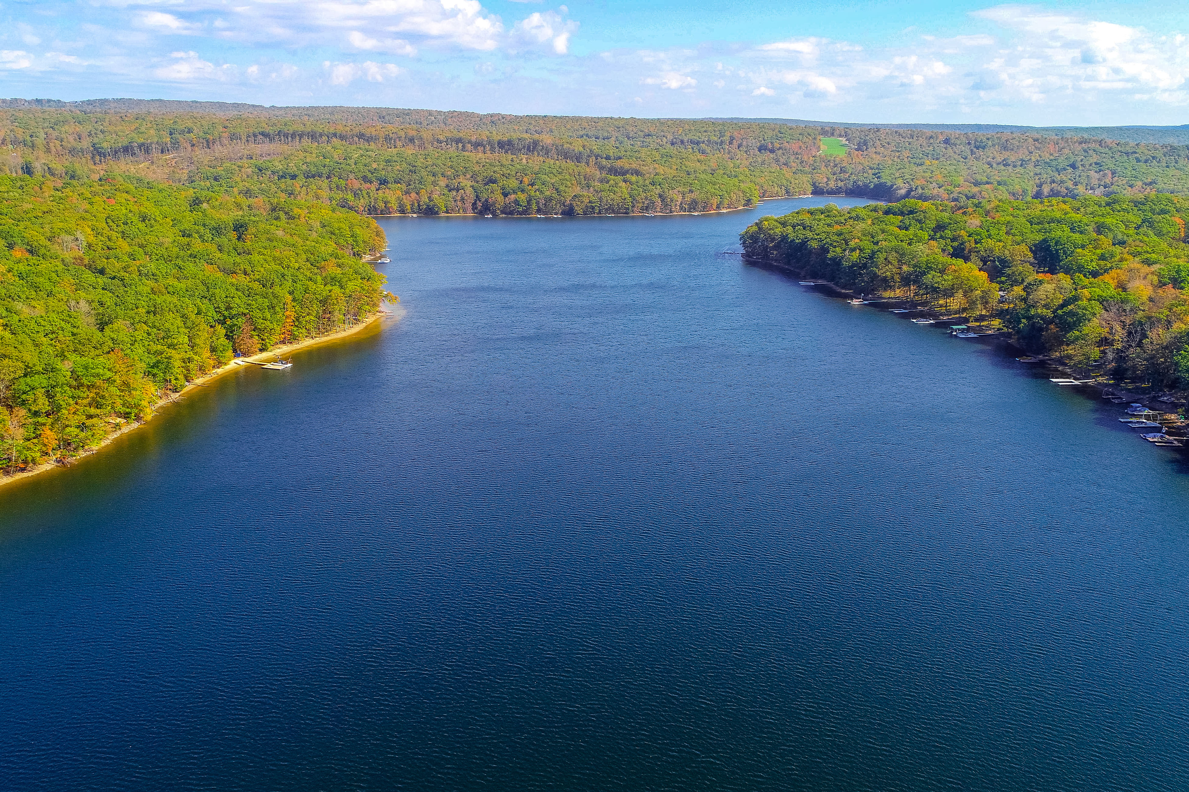 Aerial view of Deep Creek Lake, MD with deep blue waters and lush green trees during the day.