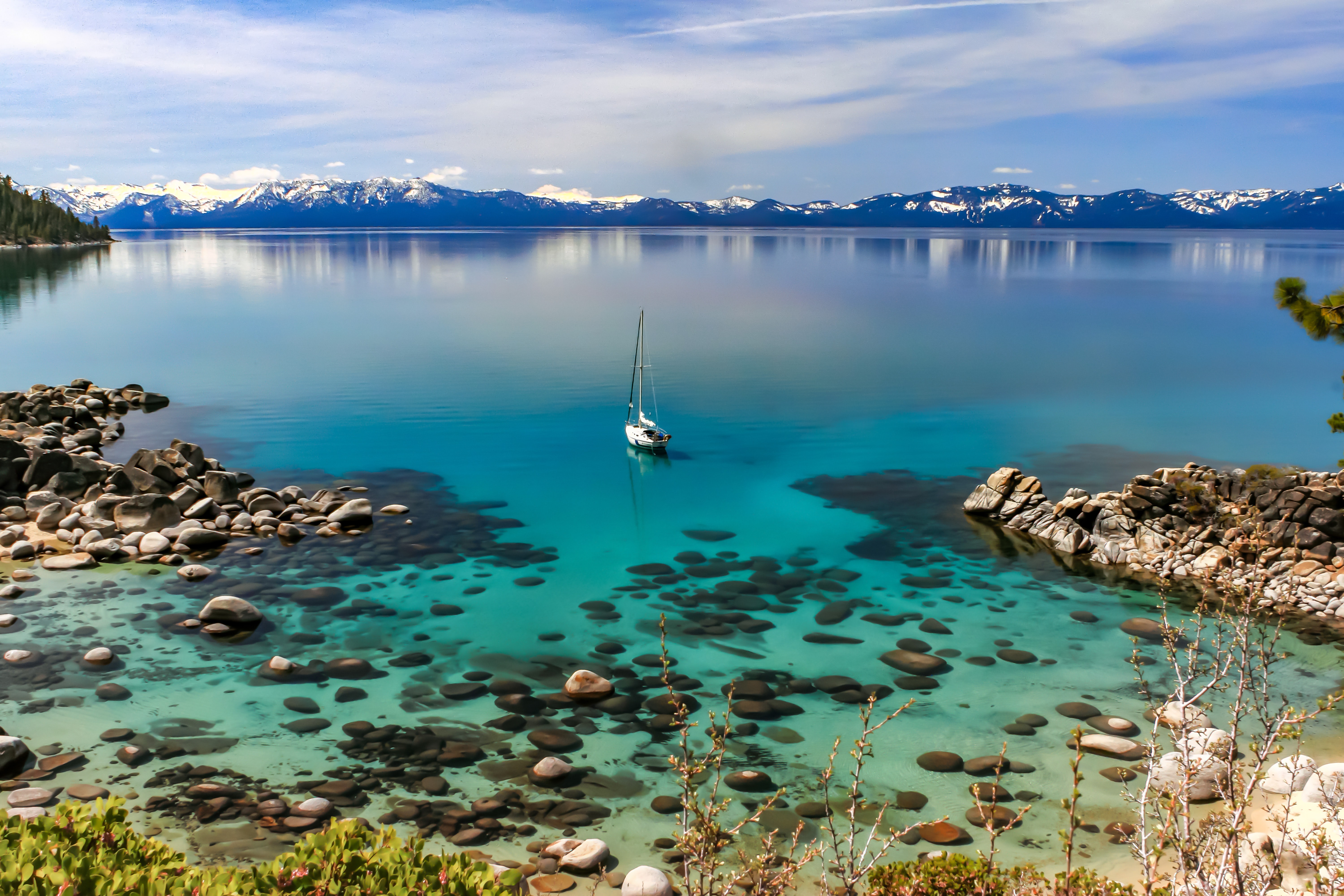 Lake Tahoe surrounded by snow-covered mountains with sailboat and crystal clear waters