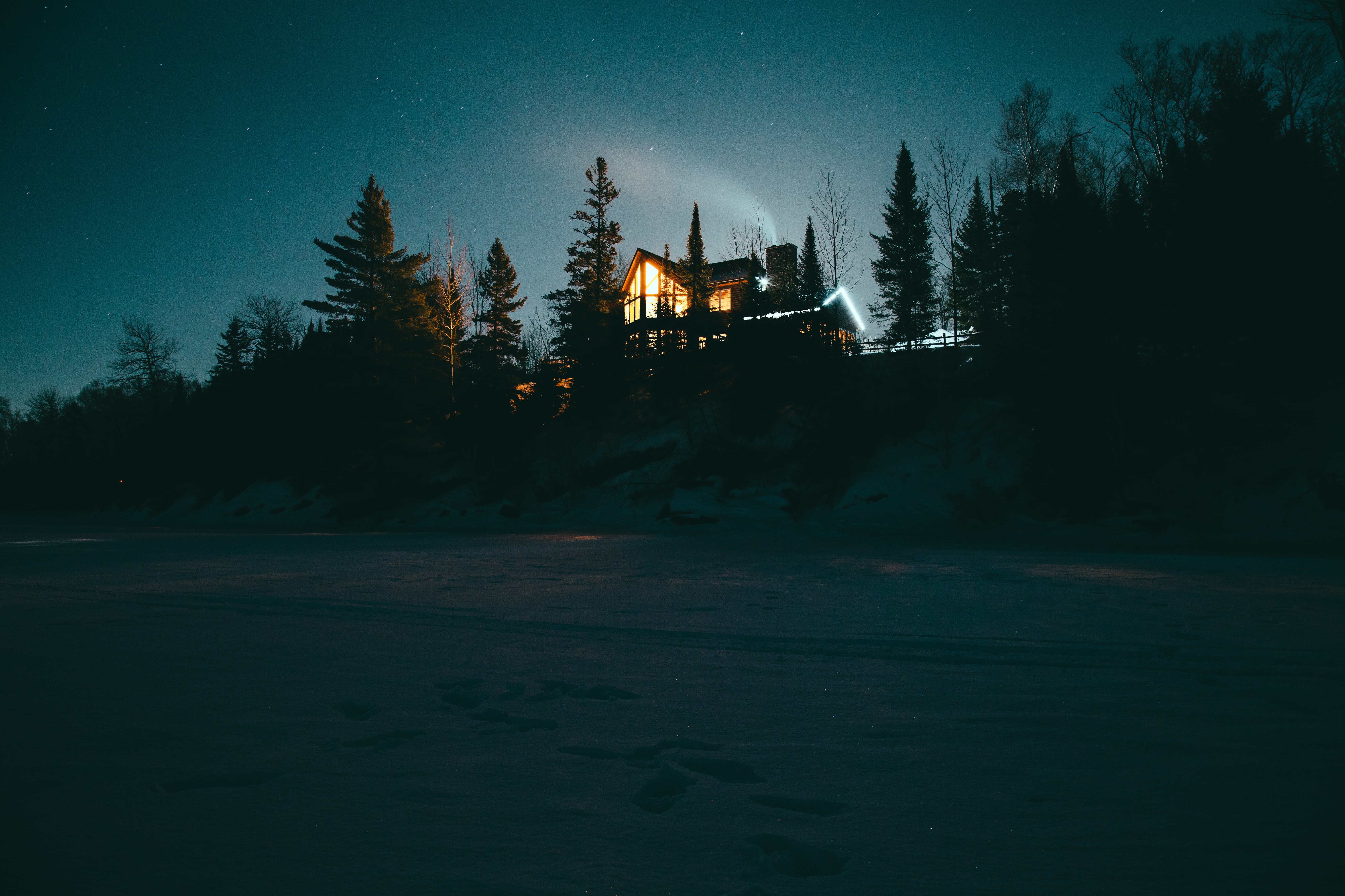 A house at night with the lights on surrounded by stars and a forest.