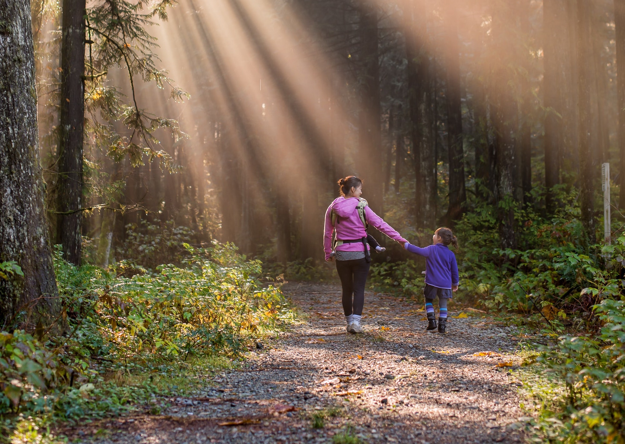mother wearing her baby while holding hands with her older daughter while hiking