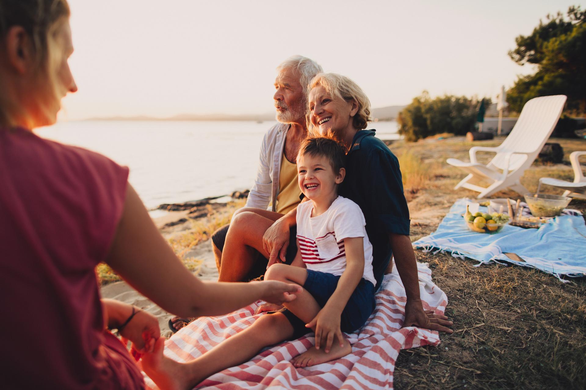 A multi-generational family hanging out by a shore sitting on beach towels.