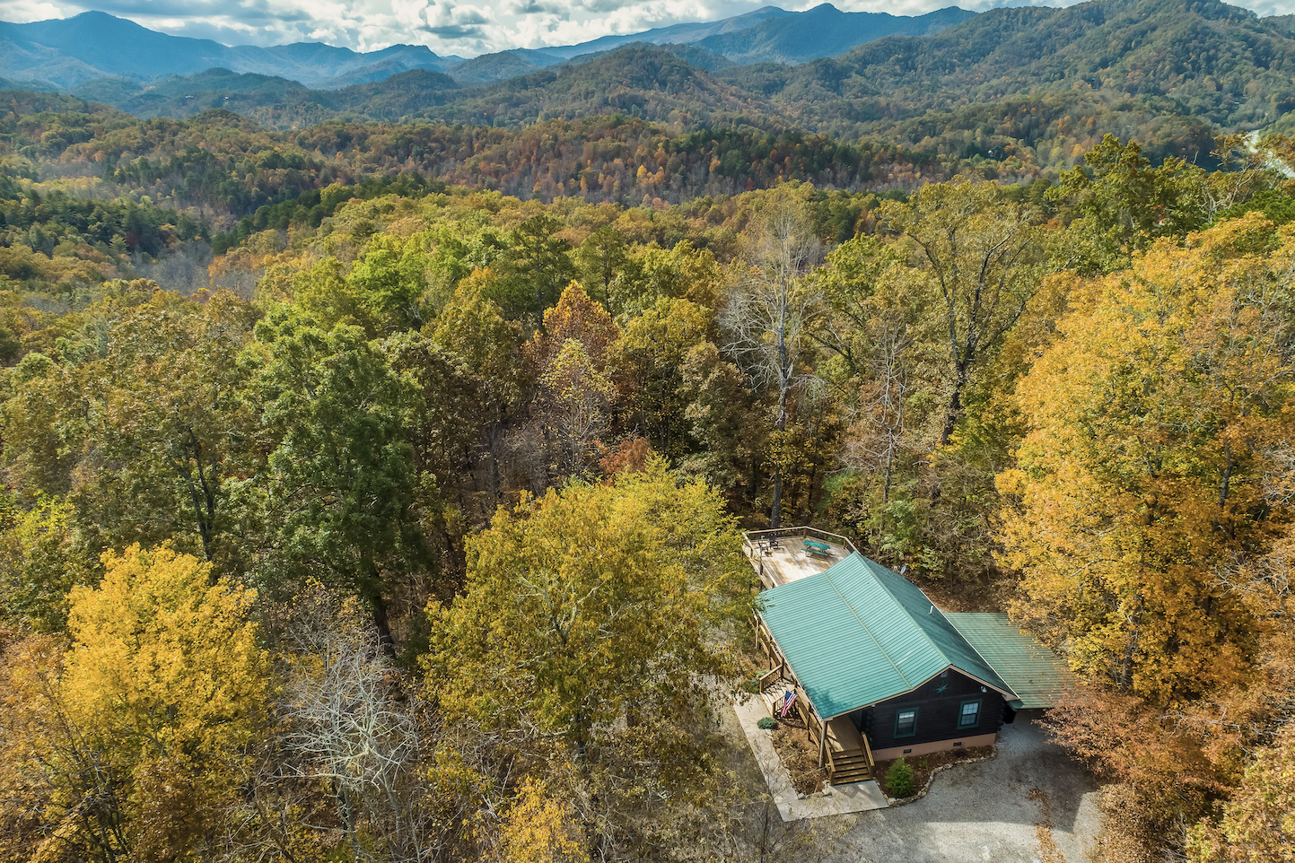 cabin with green roof surrounded by fall trees with mountains in the background in nantahala national forest