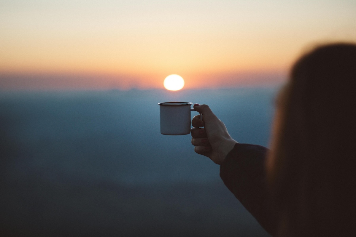 A hand holding a coffee cup overlooking a sunset.
