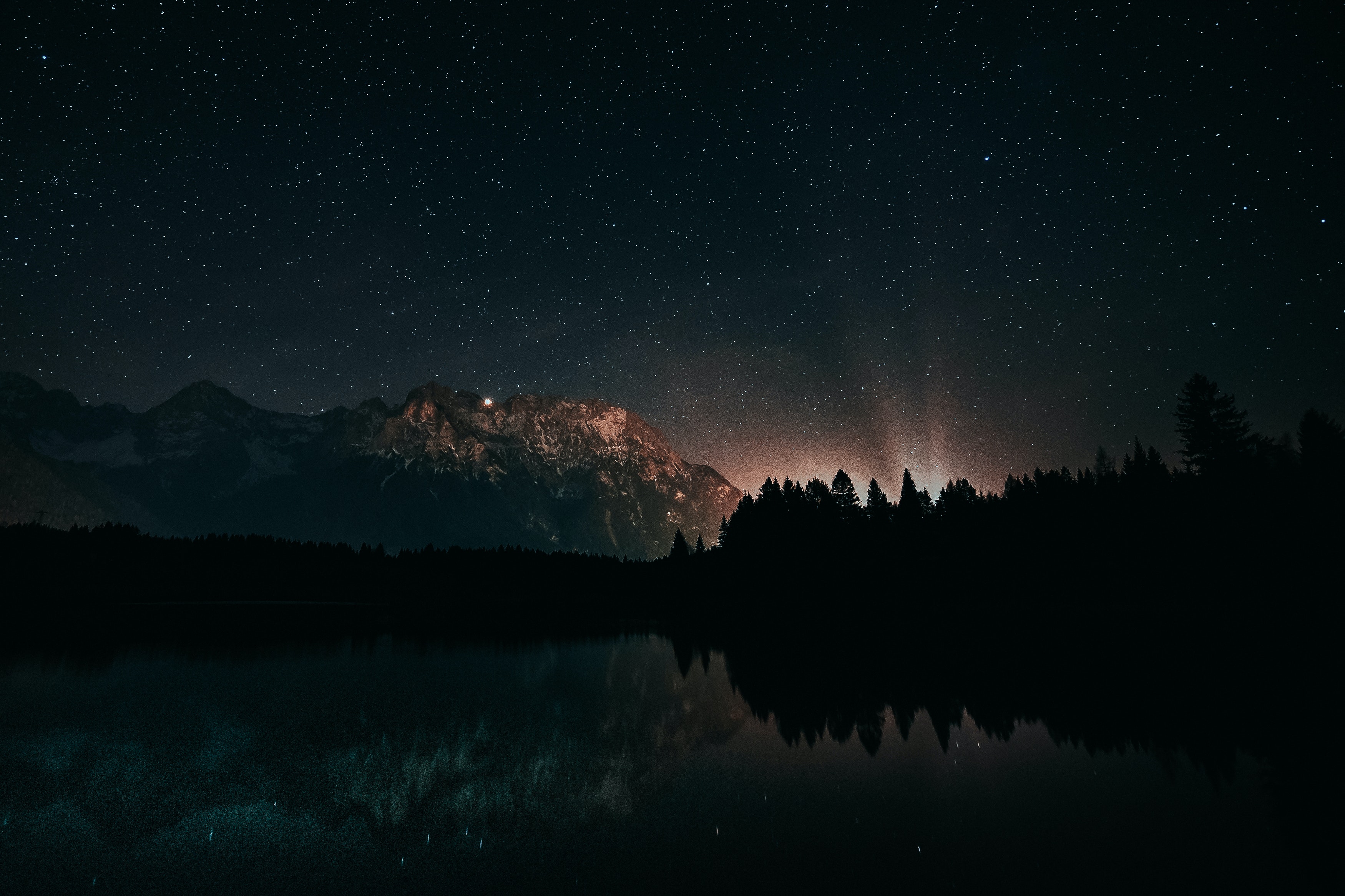 Image of a lake shadowed by a mountain with a bright light and a vast view of memorable star features.