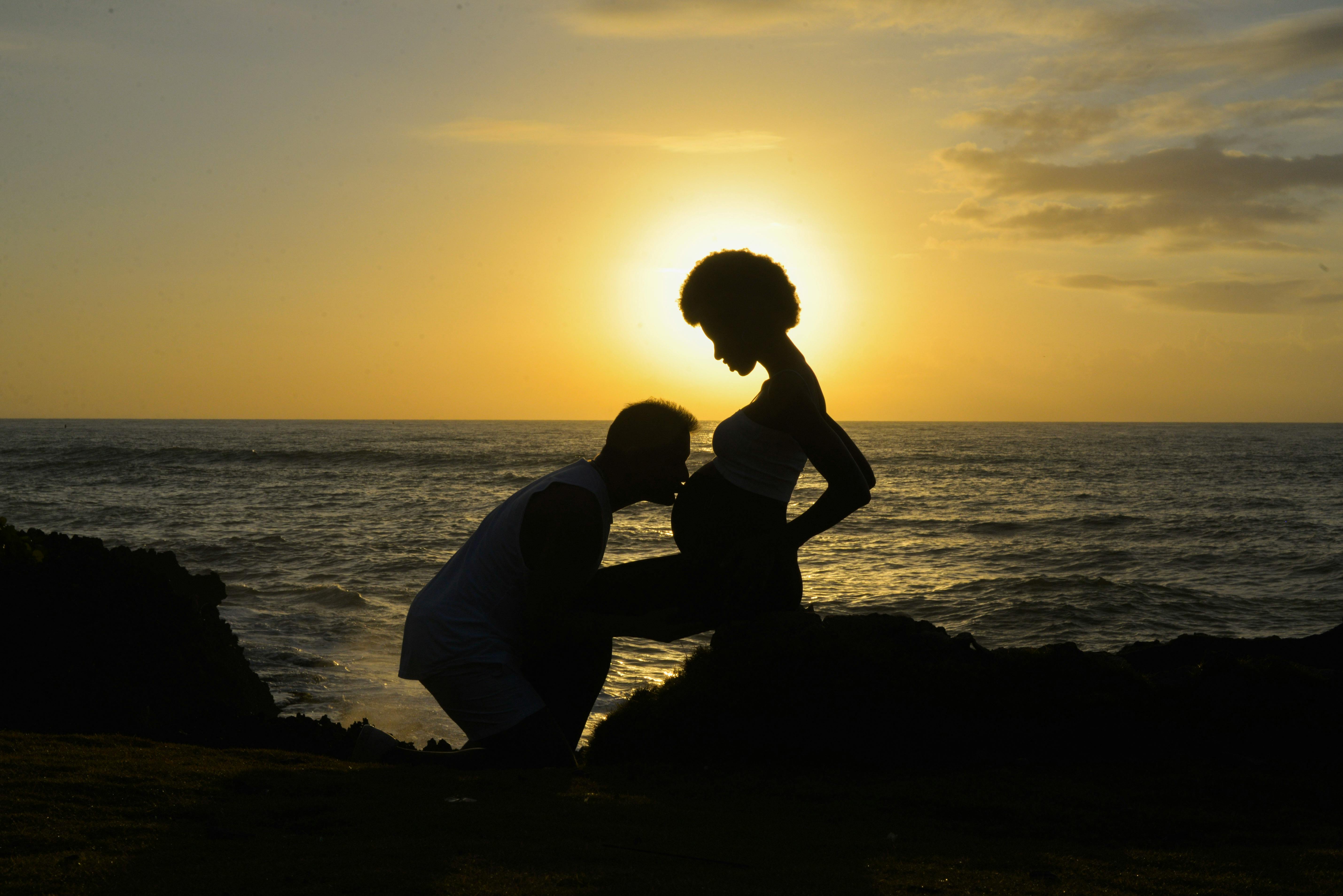A man kissing the belly of a pregnant woman at dusk.