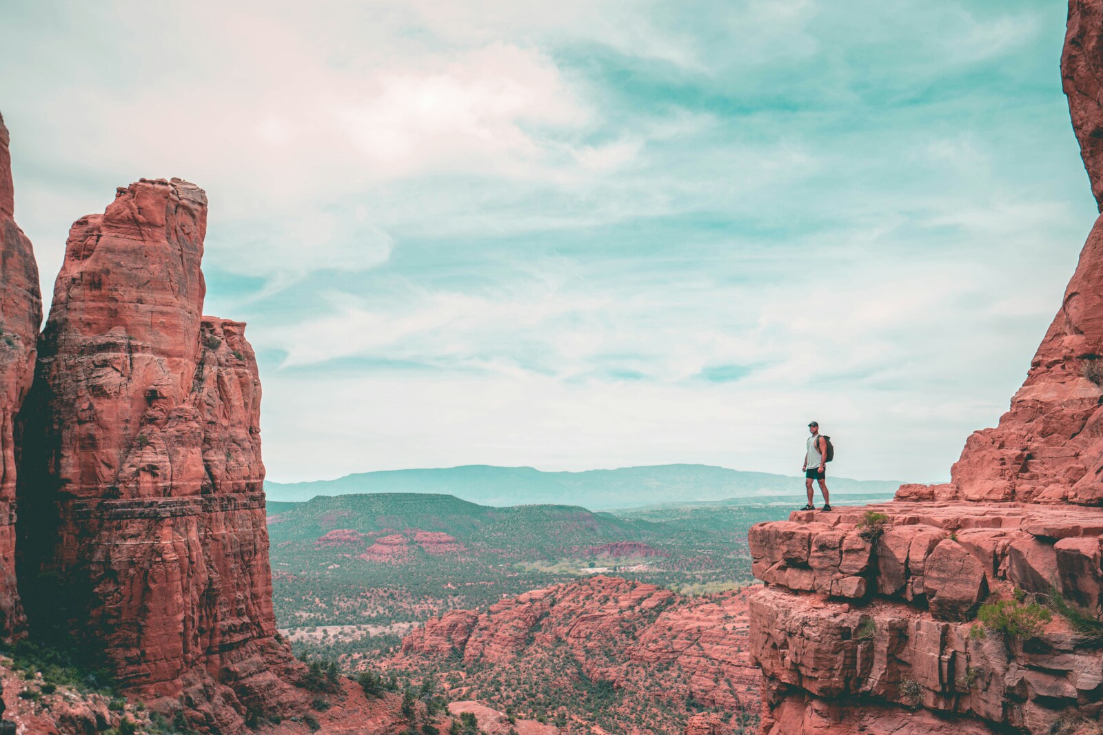 person standing by the edge of a mountain cliff overlooking red rocks
