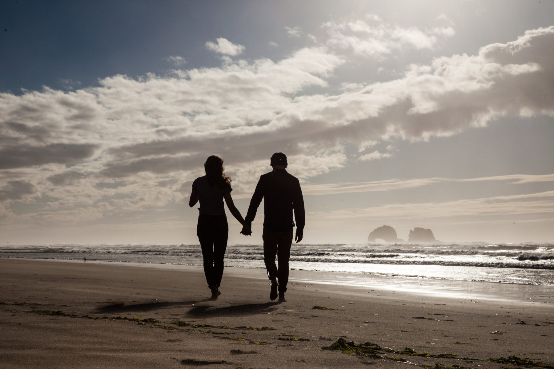 a couple holding hands walking along an oregon beach