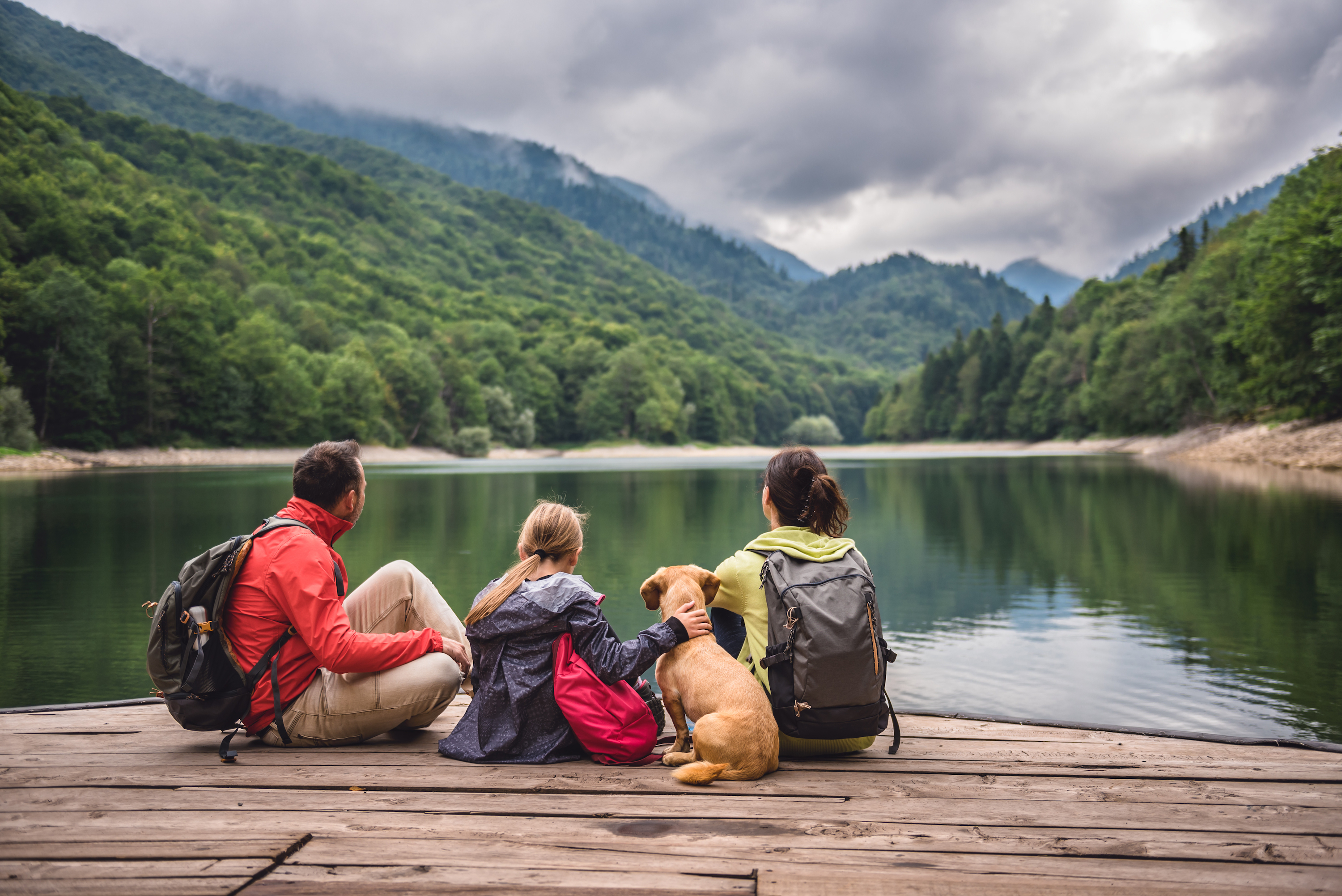 a family and their dog sitting on a dock overlooking a lake