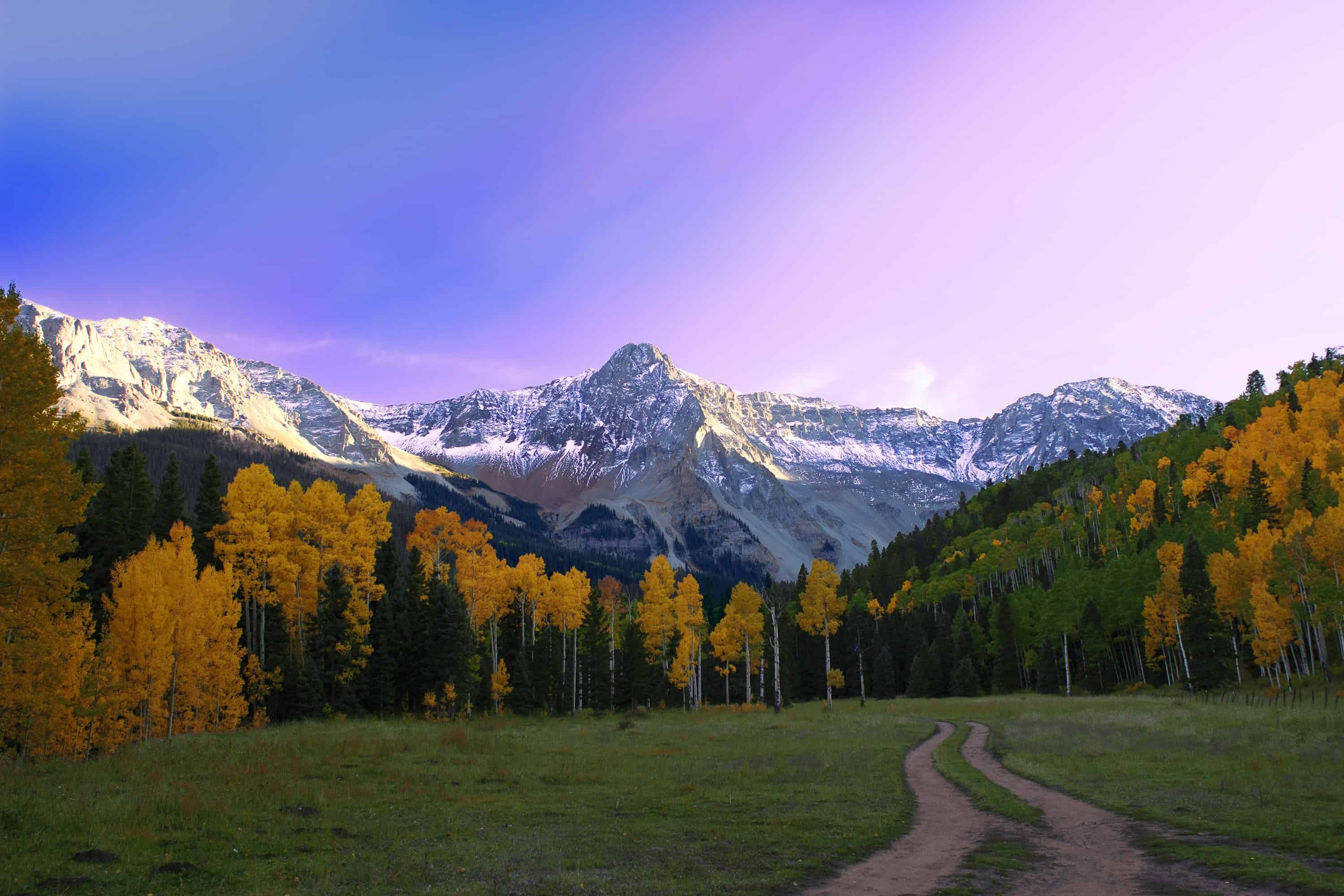 A dirt path heading towards a beautiful snow capped mountain range with a ray of sunshine in Telluride, Colorado.