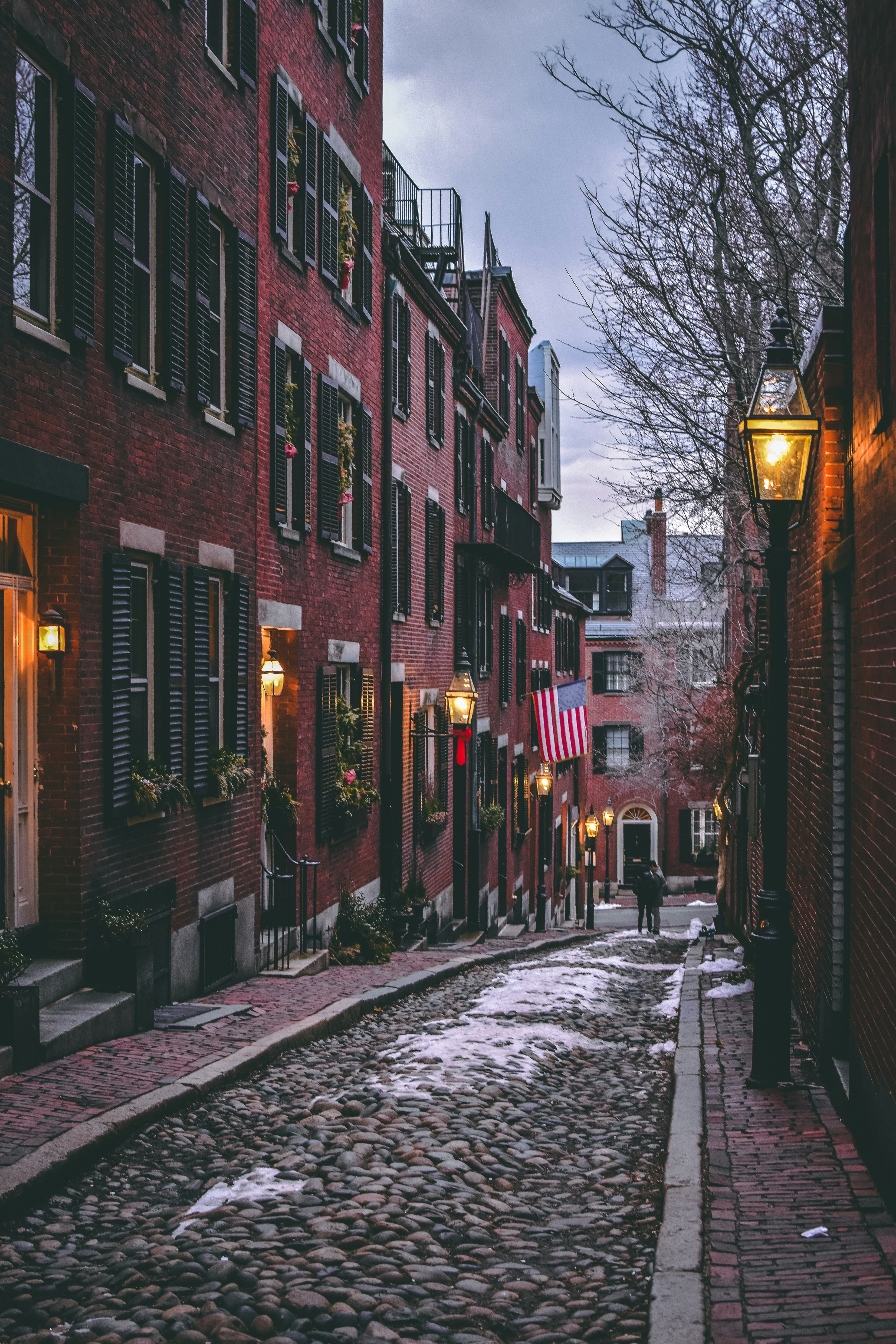 snowy cobblestone street in boston surrunded by tall brick buildings decorated for christmas