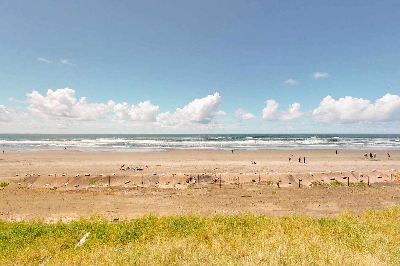 A sandy beach with people hanging out along the shore on a sunny day with white clouds